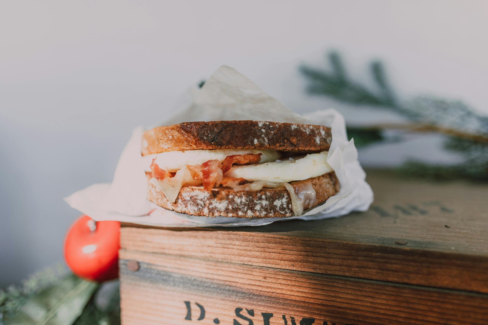 Sandwich emballé dans du papier, sur une boîte en bois, avec une pomme rouge et un brin de sapin.