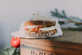 Un sandwich au fromage grillé emballé dans du papier, posé sur une boîte en bois avec une pomme rouge