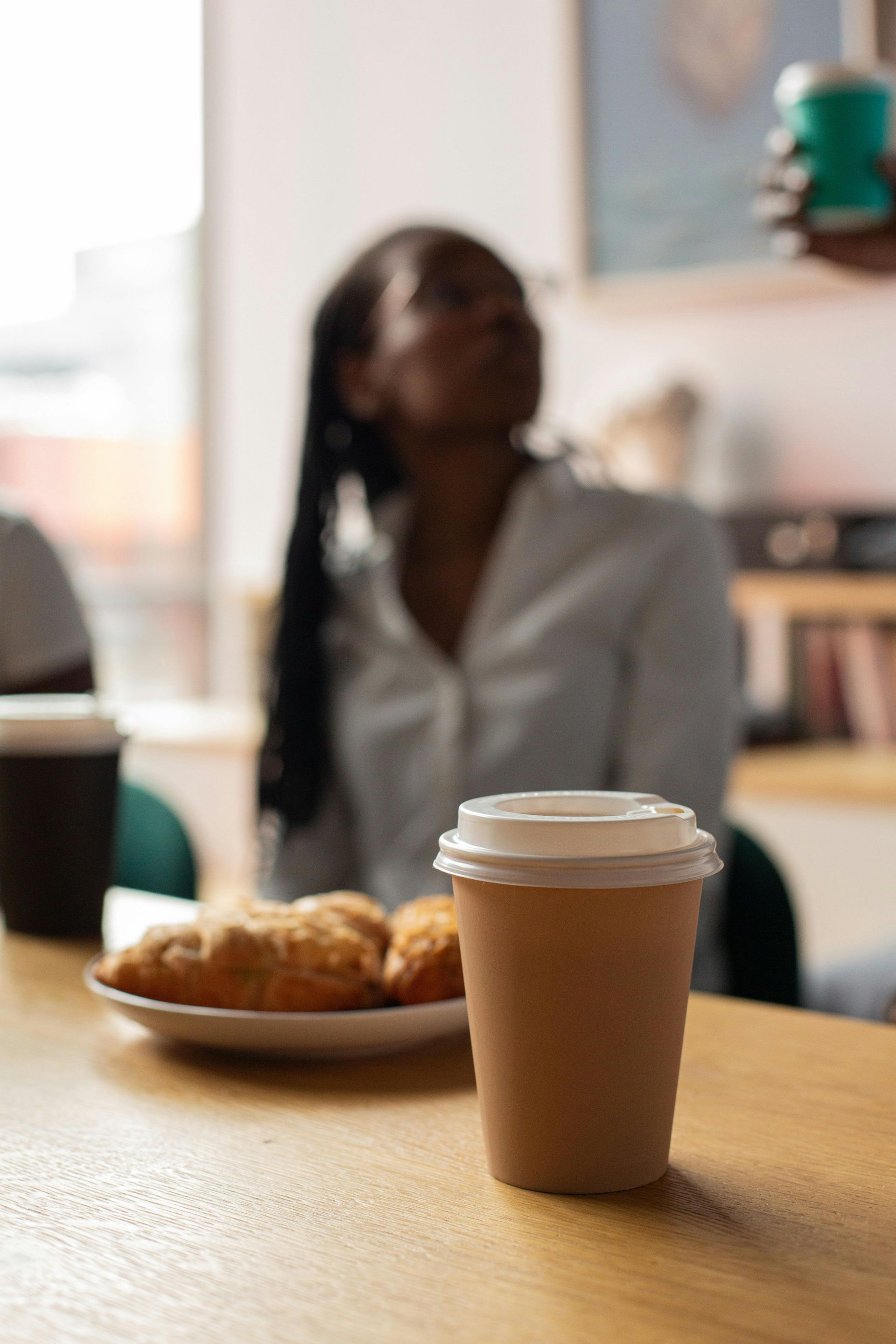 Coffee cup and pastry on a table, with a blurred seated person in the background.
