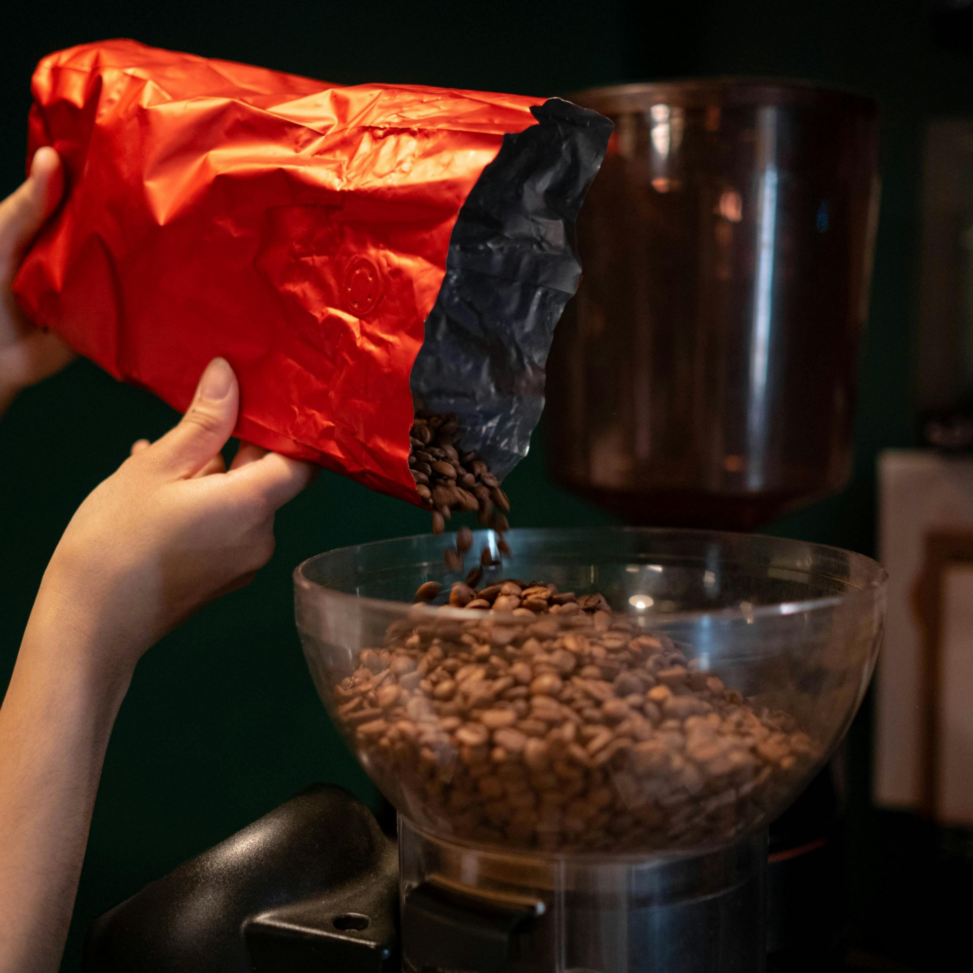 Versement manuel de grains de café d'un sachet rouge dans la trémie du moulin.