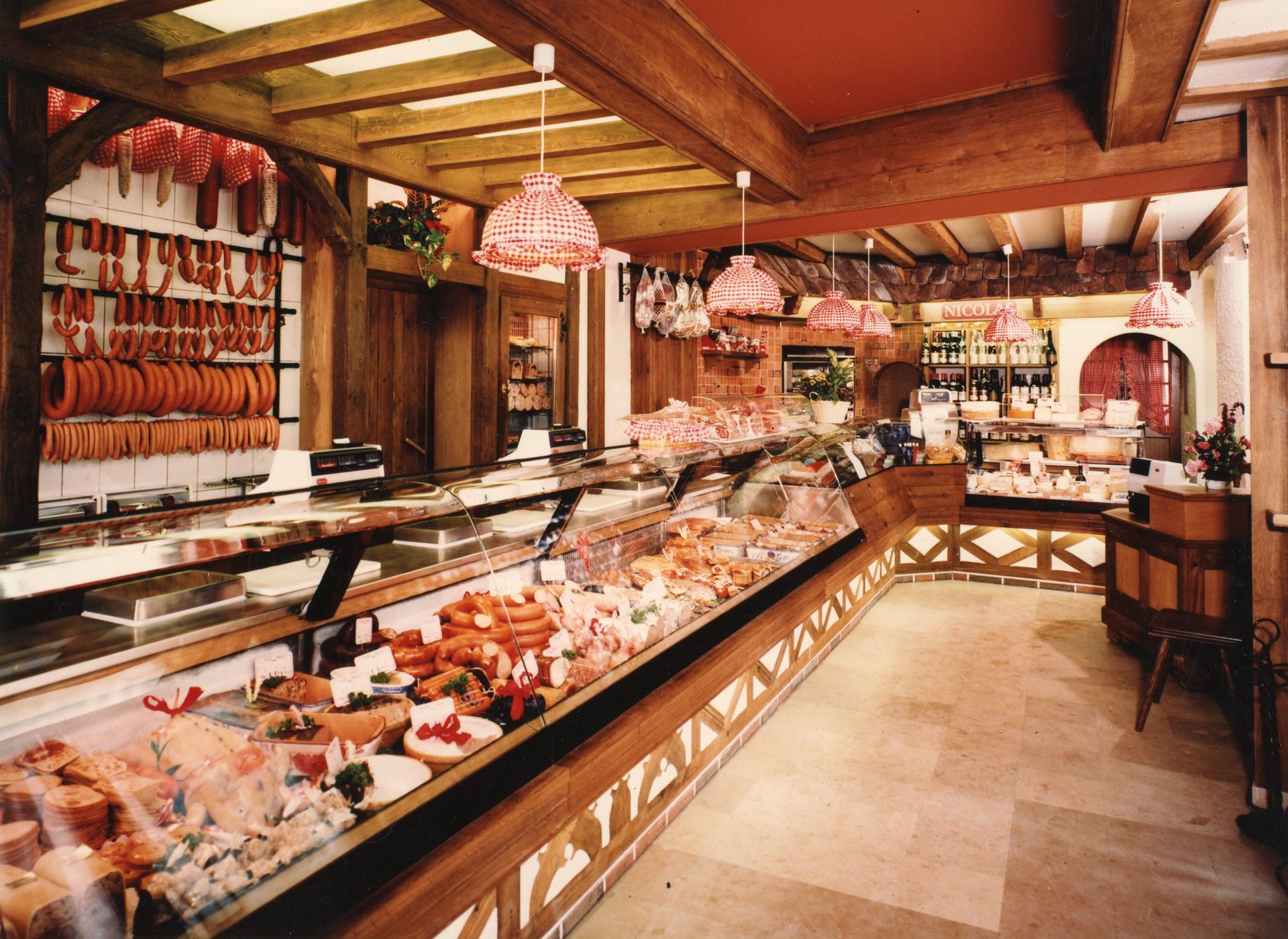 Élégant comptoir de charcuterie avec viandes suspendues, pâtisseries et intérieur chaleureux en bois et marbre