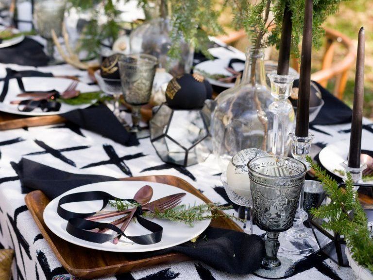 A table setting with plates , glasses , candles and a black and white table cloth.