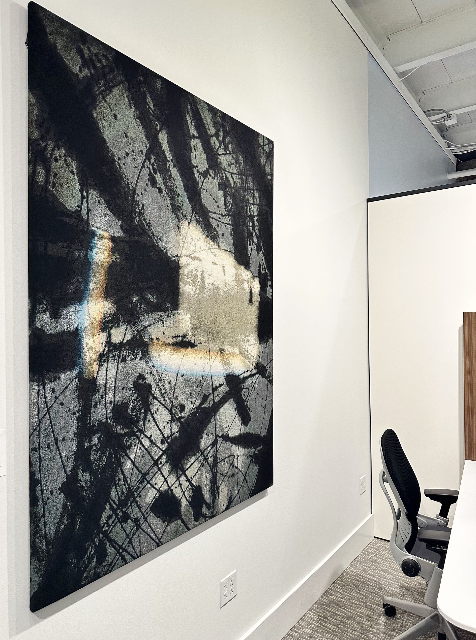 A large painting is hanging on a white wall in a room.