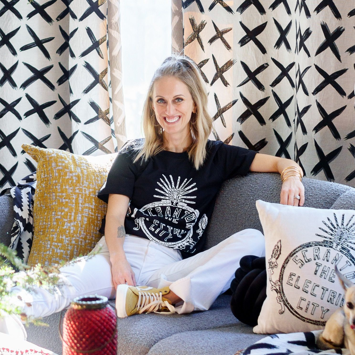 A woman is sitting on a couch wearing a black shirt and white pants.