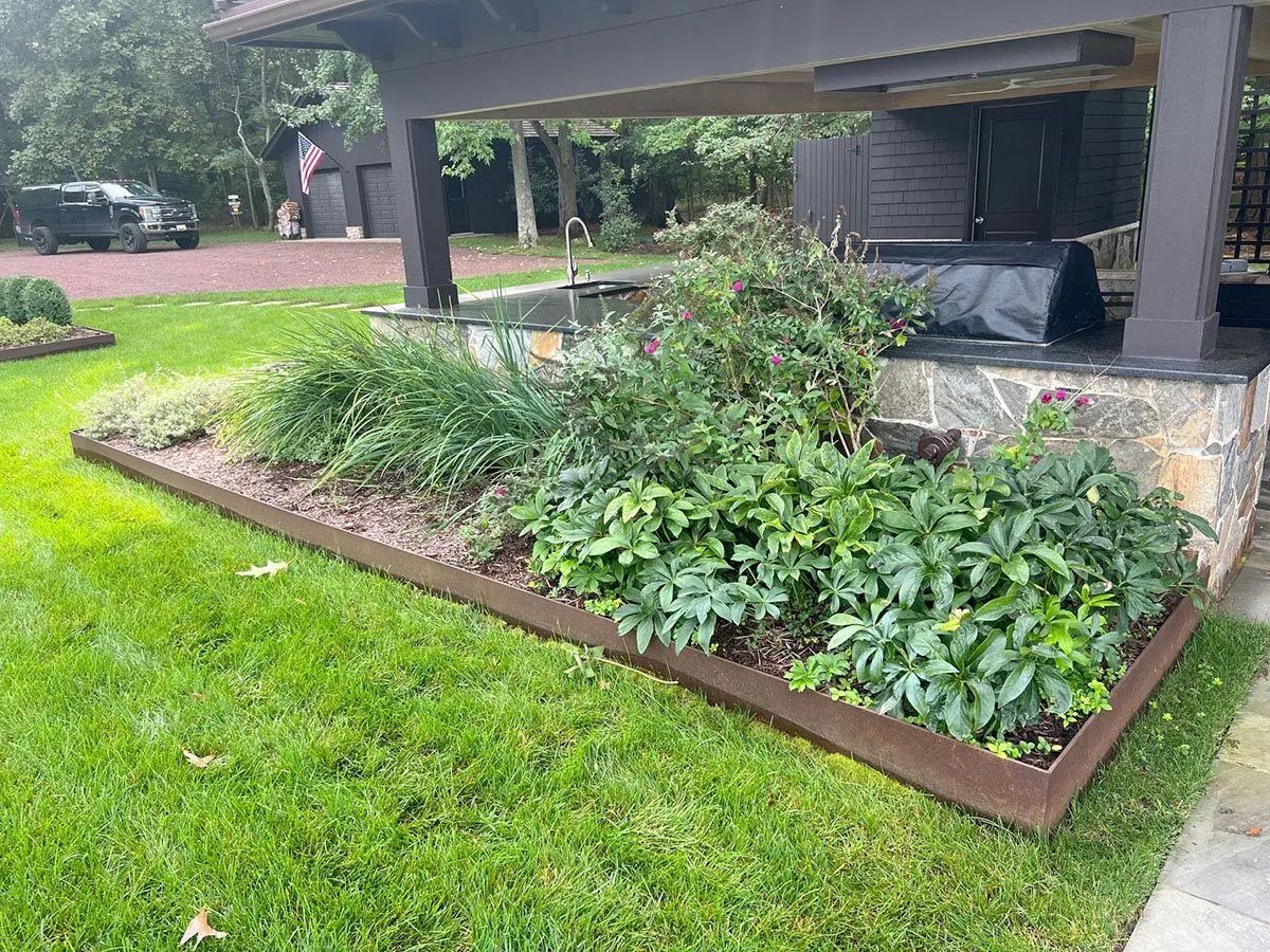 Raised garden bed with green plants beside a pavilion on a lawn