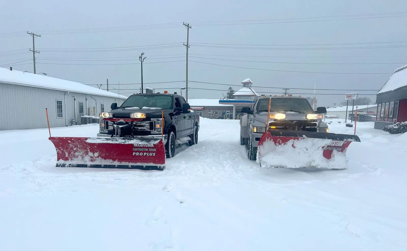 Two snow plows clearing a snowy street in a white winter scene
