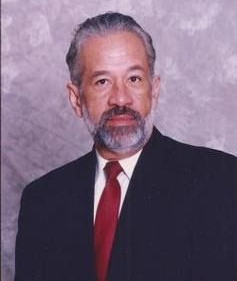 Portrait of a man in a dark suit with a red tie against a mottled gray background