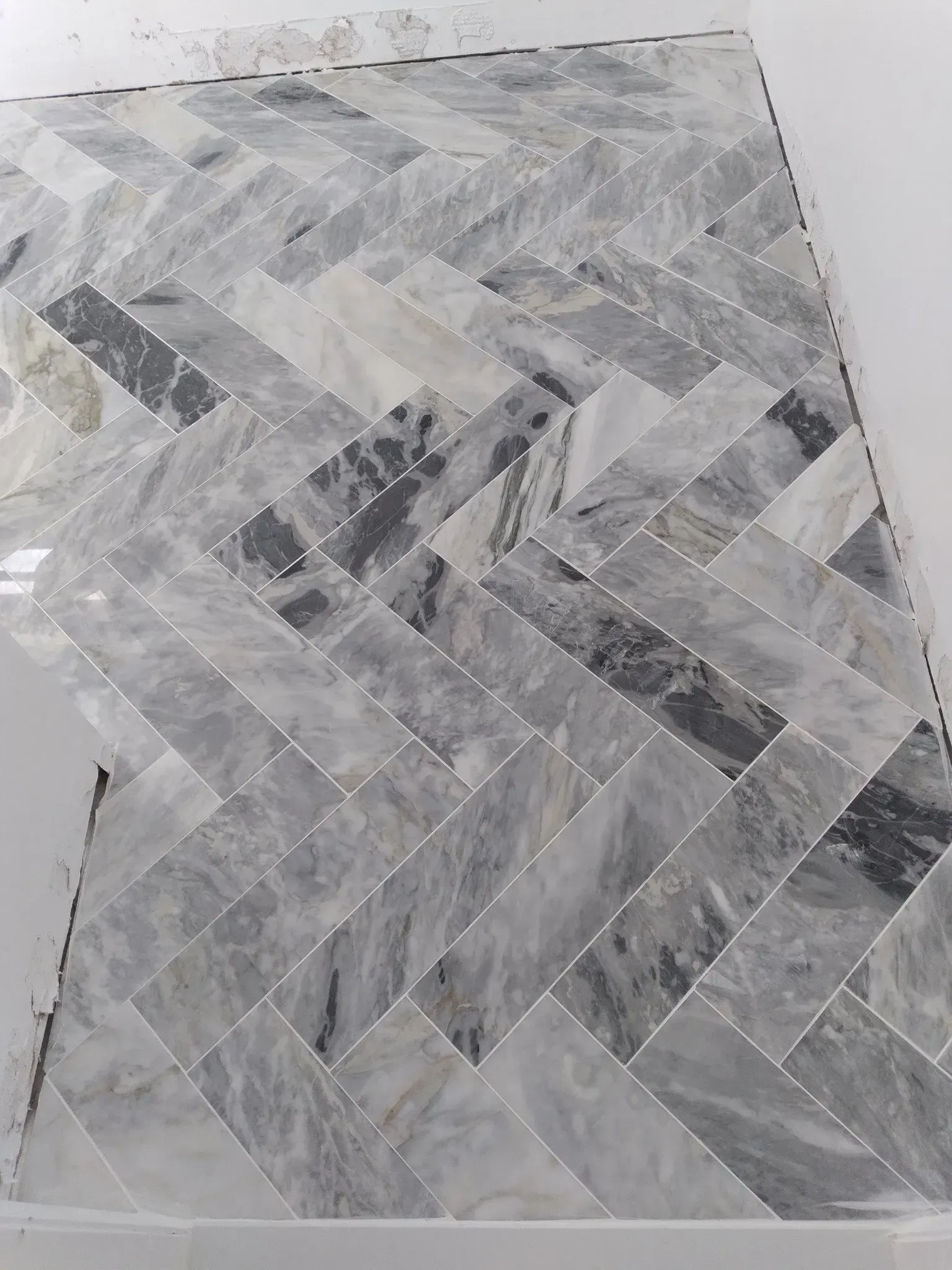 Gray herringbone-patterned tile or wood flooring sample with varied light and dark tones