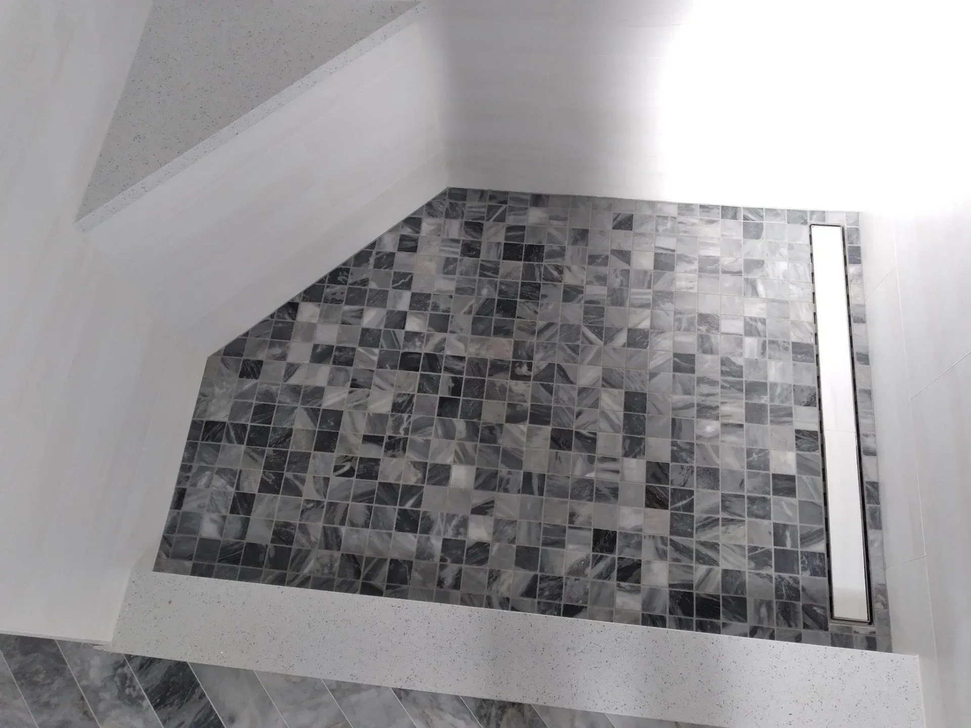 Empty stairwell landing with gray mosaic tile floor and white walls