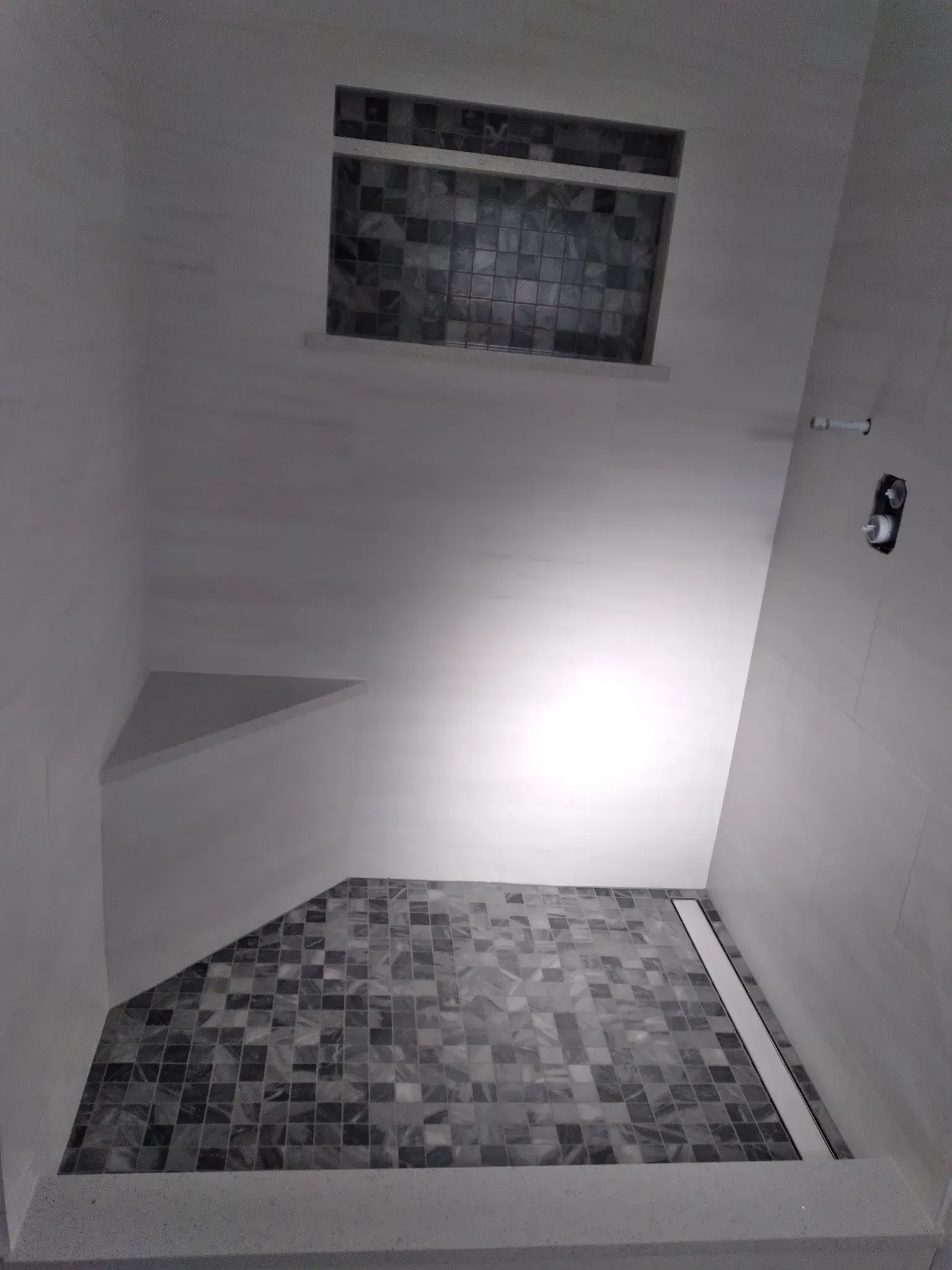 Small tiled shower corner with gray walls, white floor, and a frosted window.