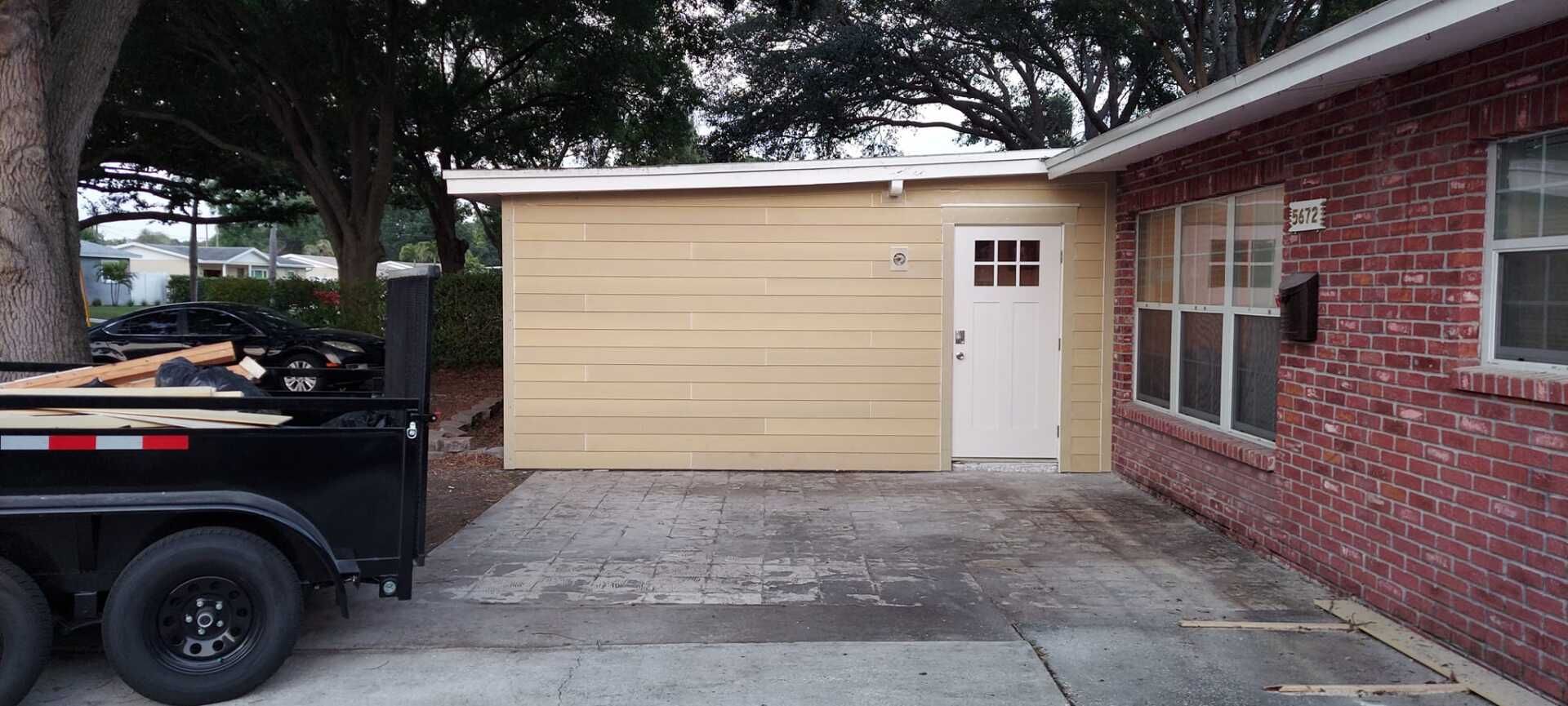 Driveway beside a brick house with a beige garage door and a black trailer parked on the left