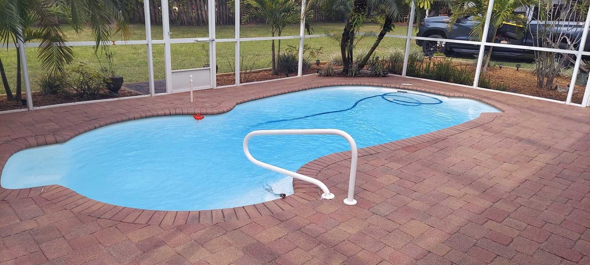Empty backyard pool with blue water, surrounded by a brick patio and white fence.