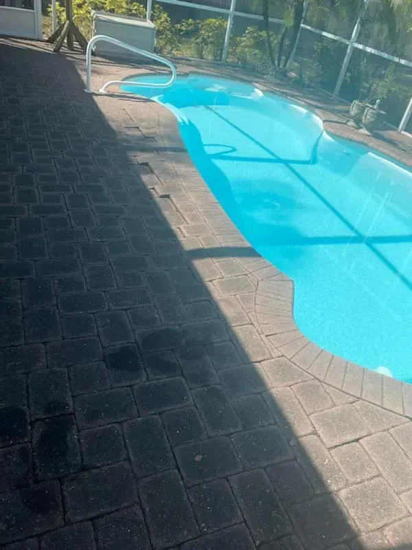 Backyard swimming pool with bright blue water beside a dark stone patio and metal handrail
