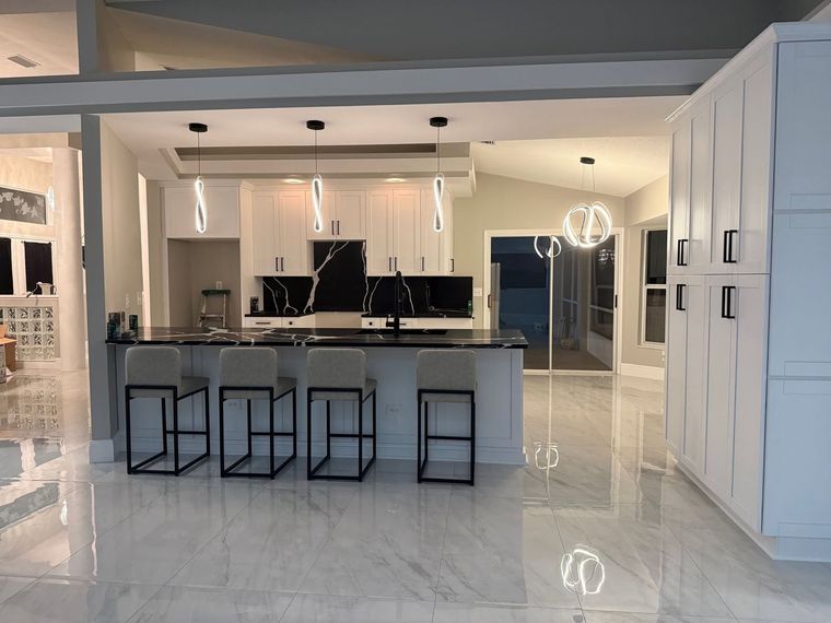 Modern white kitchen with black island, bar stools, glossy floor, and pendant lights Modern white kitchen with black island, bar stools, glossy floor, and pendant lights