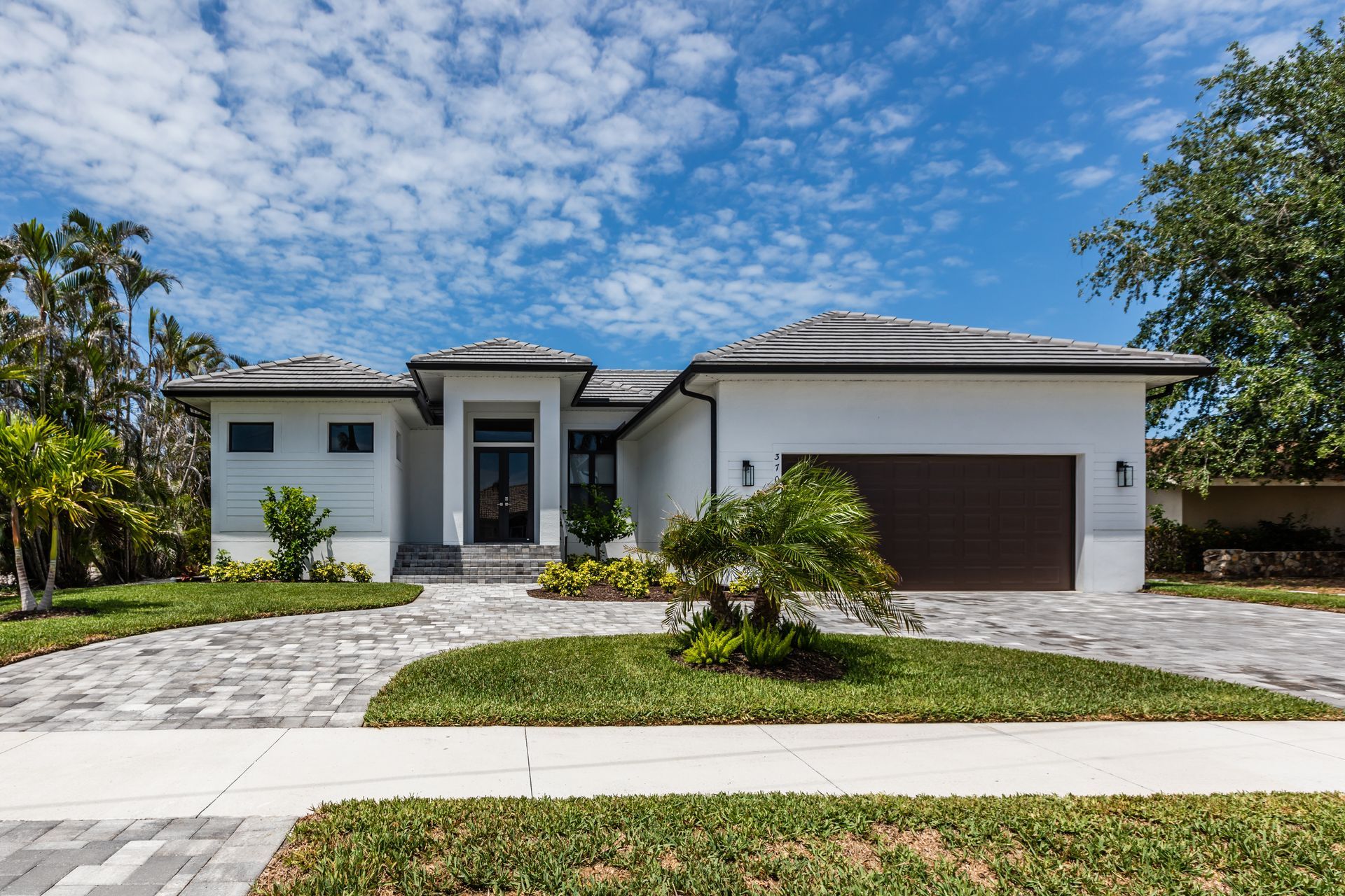 Modern single-story white house with a brown garage, front lawn, and palm trees under a blue sky Modern single-story white house with a brown garage, front lawn, and palm trees under a blue sky