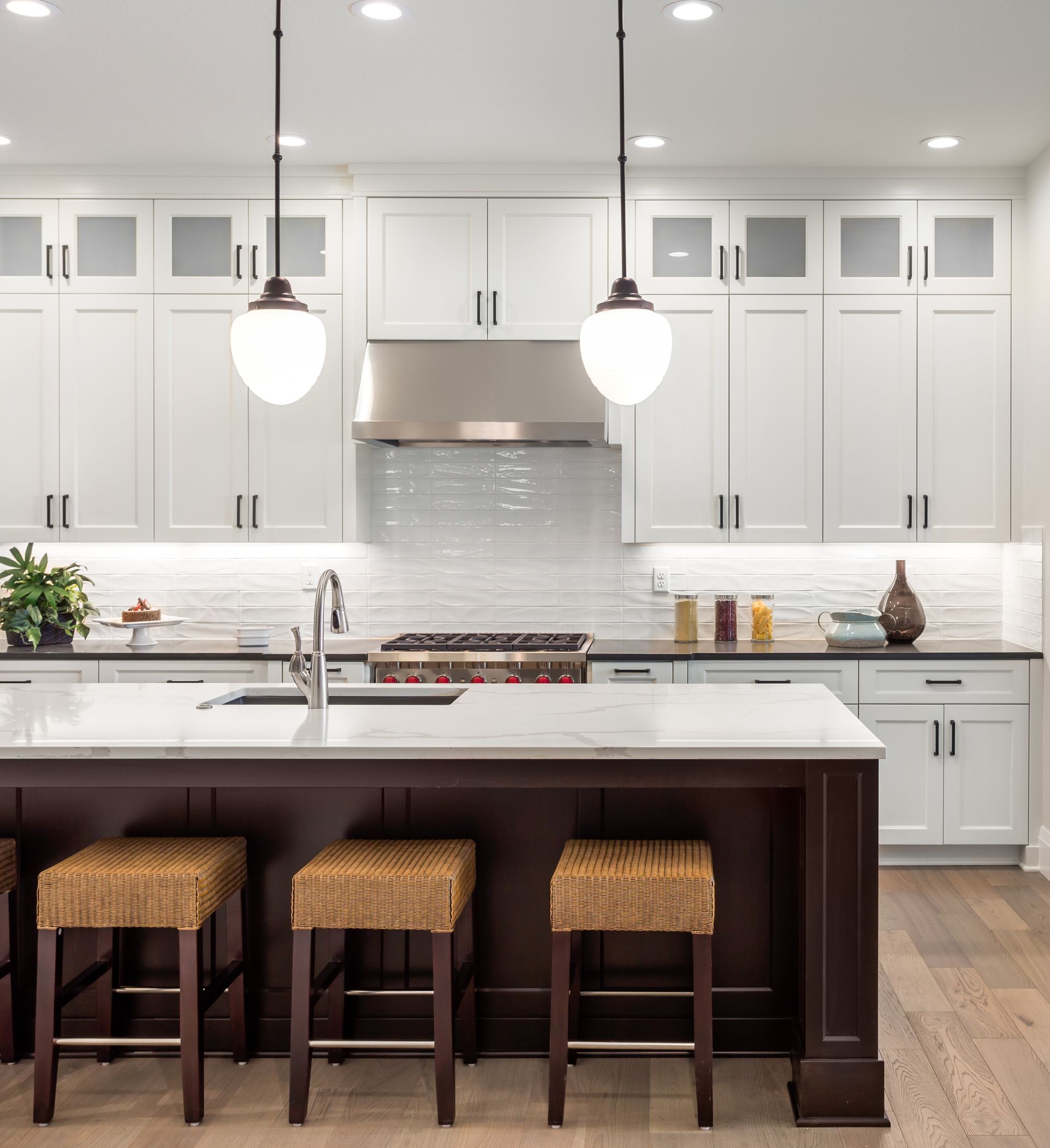 Bright white modern kitchen with island, three woven stools, pendant lights, and stainless steel range hood Bright white modern kitchen with island, three woven stools, pendant lights, and stainless steel range hood