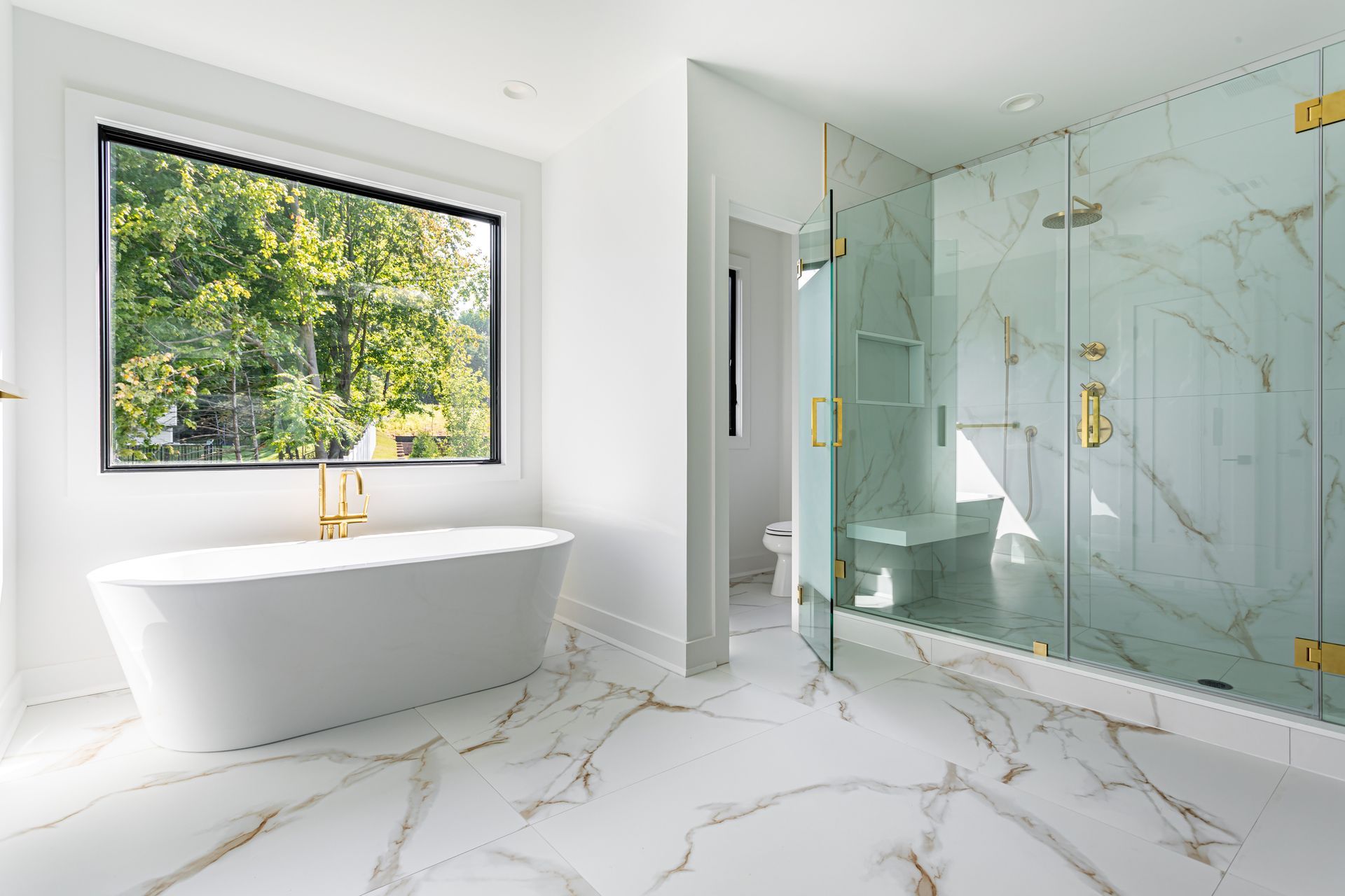 Bright modern bathroom with white marble, freestanding tub, and glass walk-in shower by a window. Bright modern bathroom with white marble, freestanding tub, and glass walk-in shower by a window.
