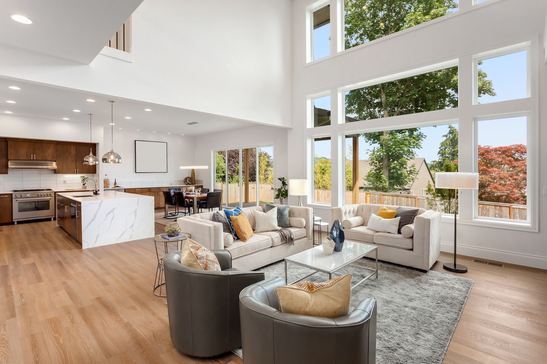 Bright open-concept living room with gray sofas, white walls, wood floors, and large windows Bright open-concept living room with gray sofas, white walls, wood floors, and large windows
