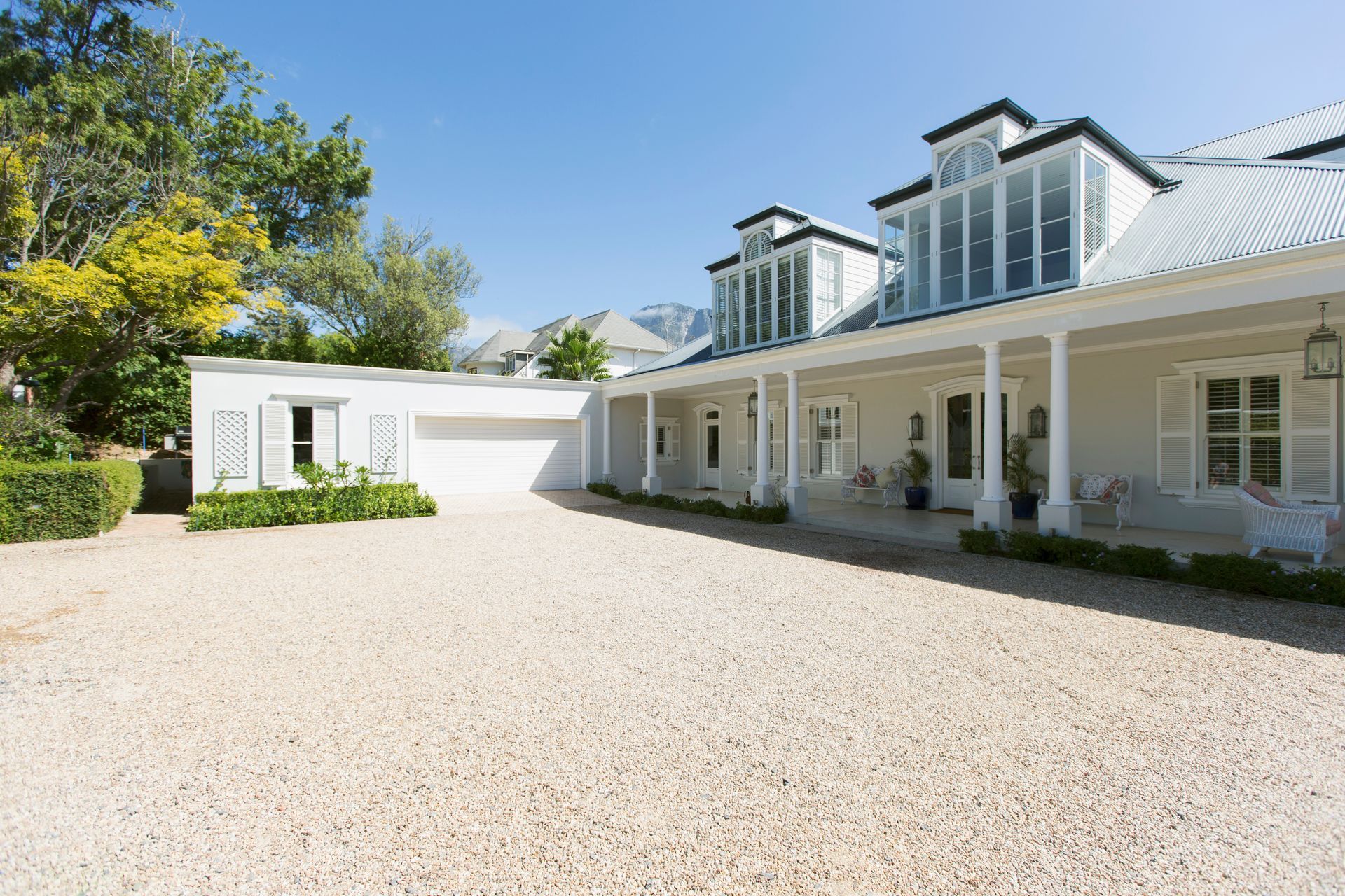 White house with dormer windows and a gravel driveway, viewed from the front in bright sunlight White house with dormer windows and a gravel driveway, viewed from the front in bright sunlight
