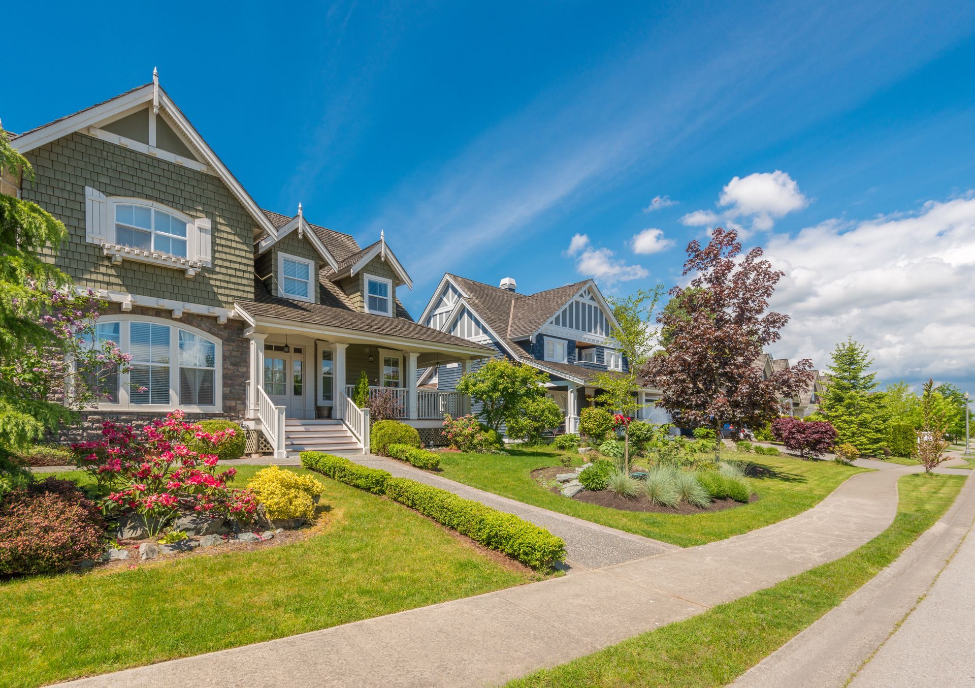 Row of suburban houses with manicured lawns, flowerbeds, and a curving sidewalk under a bright blue sky Row of suburban houses with manicured lawns, flowerbeds, and a curving sidewalk under a bright blue sky