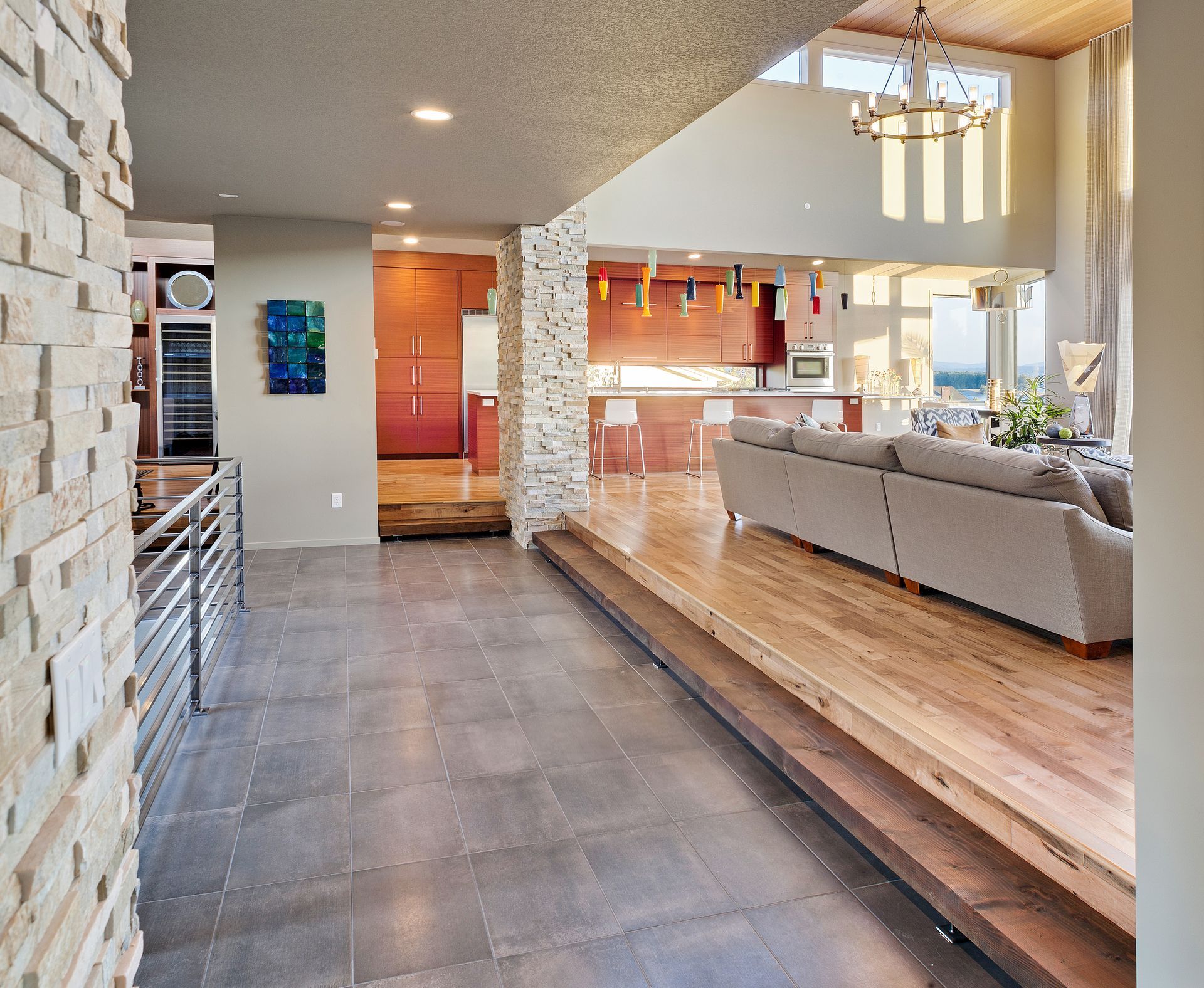 Modern open-concept kitchen and living room with gray tile, wood accents, and beige sectional sofa Modern open-concept kitchen and living room with gray tile, wood accents, and beige sectional sofa