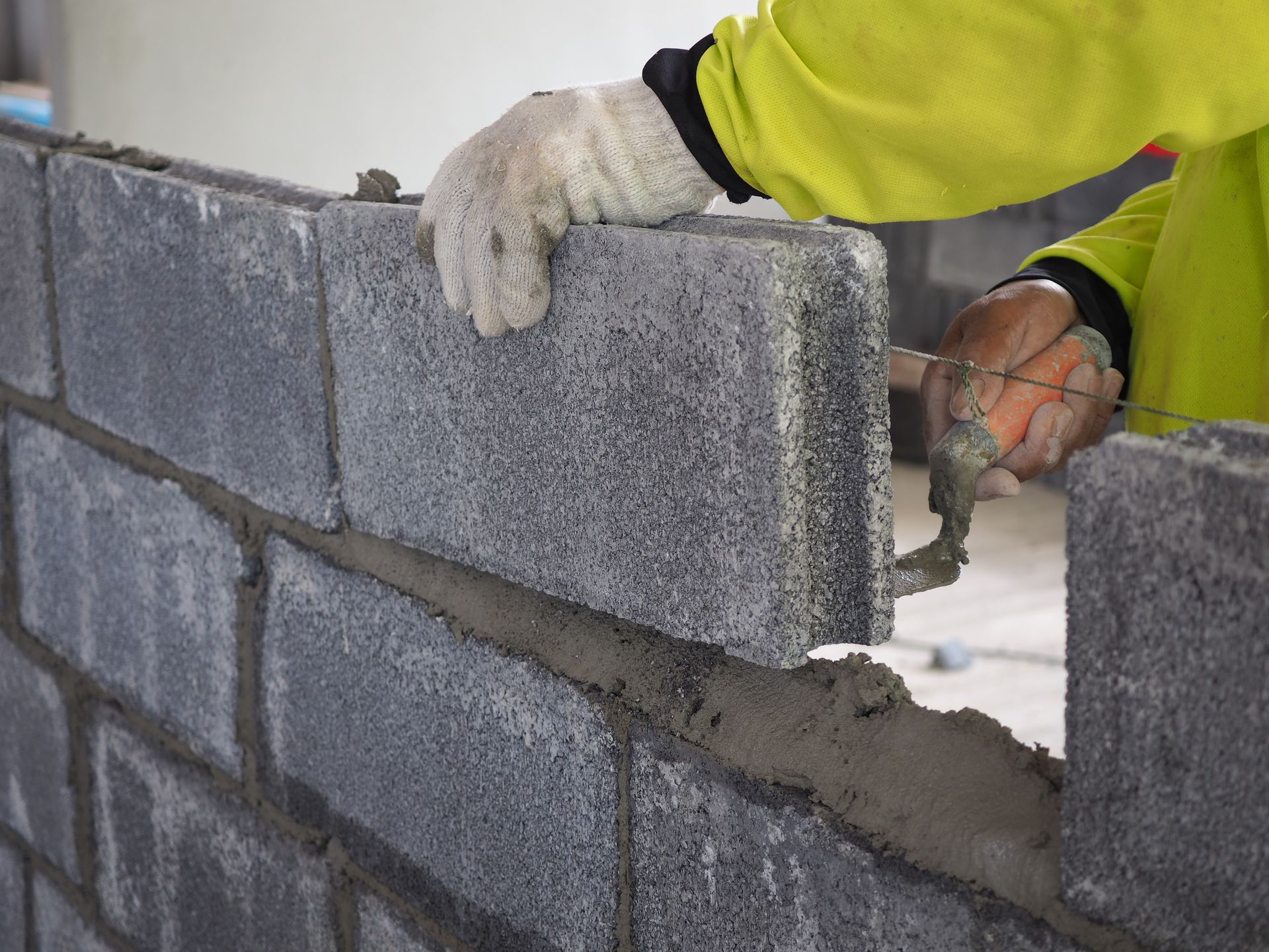 Worker laying gray cinder blocks with mortar on a wall outdoors Worker laying gray cinder blocks with mortar on a wall outdoors