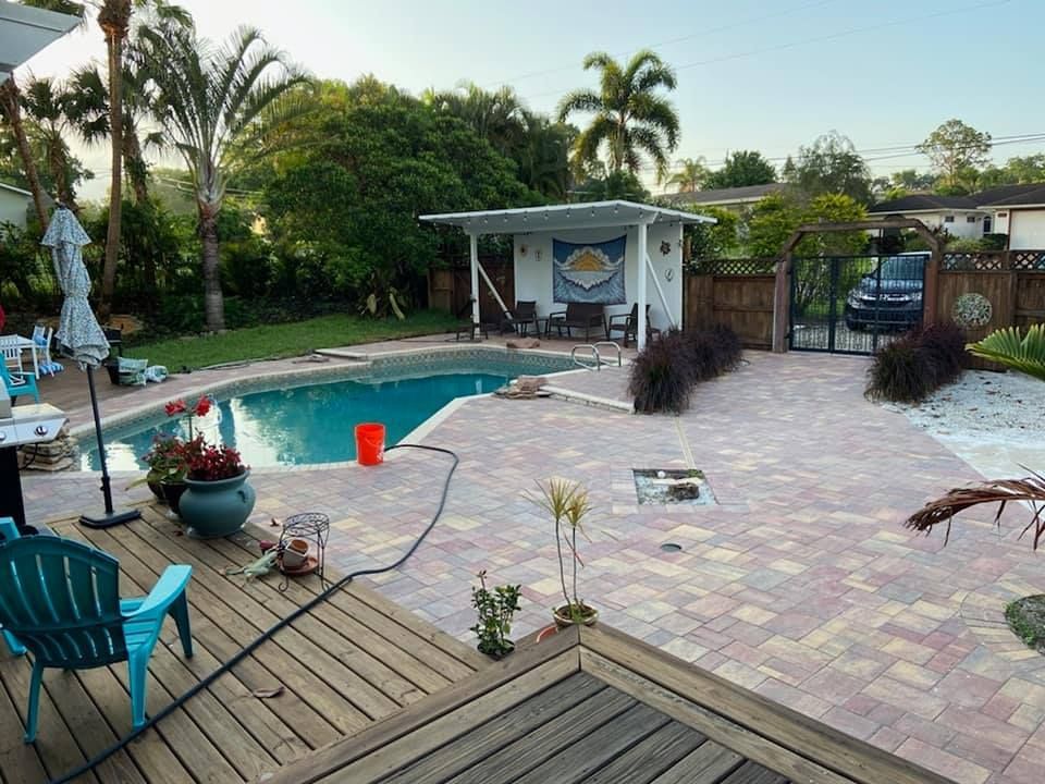 Backyard pool with patio, lounge chairs, tropical plants, and a small cabana at sunset