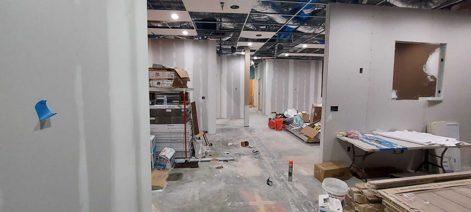 Unfinished office hallway with exposed ceiling, debris, and construction materials scattered on the floor.