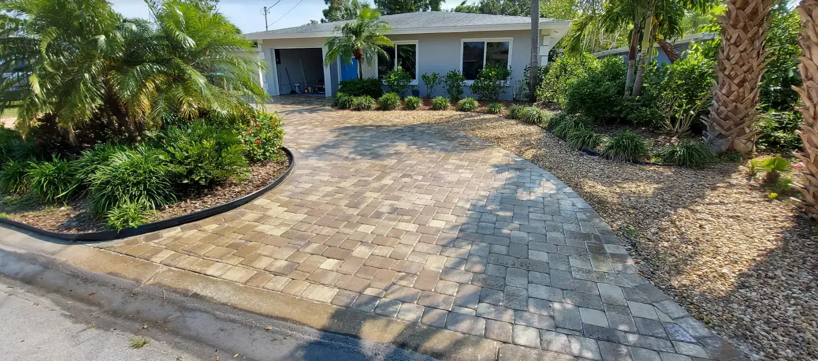 Stone driveway leading to a house entrance, with palm trees and landscaped greenery on both sides