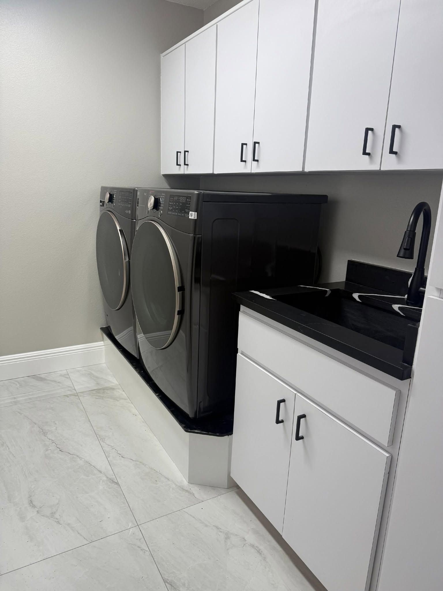 Laundry room with white cabinets, black countertop, and silver washer and dryer on a light tile floor Laundry room with white cabinets, black countertop, and silver washer and dryer on a light tile floor