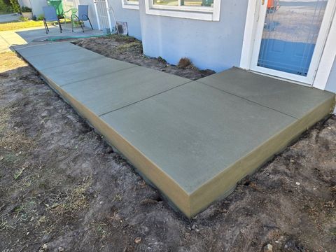 Concrete front walkway and porch slab beside a blue house, bordered by bare dirt. Concrete front walkway and porch slab beside a blue house, bordered by bare dirt.