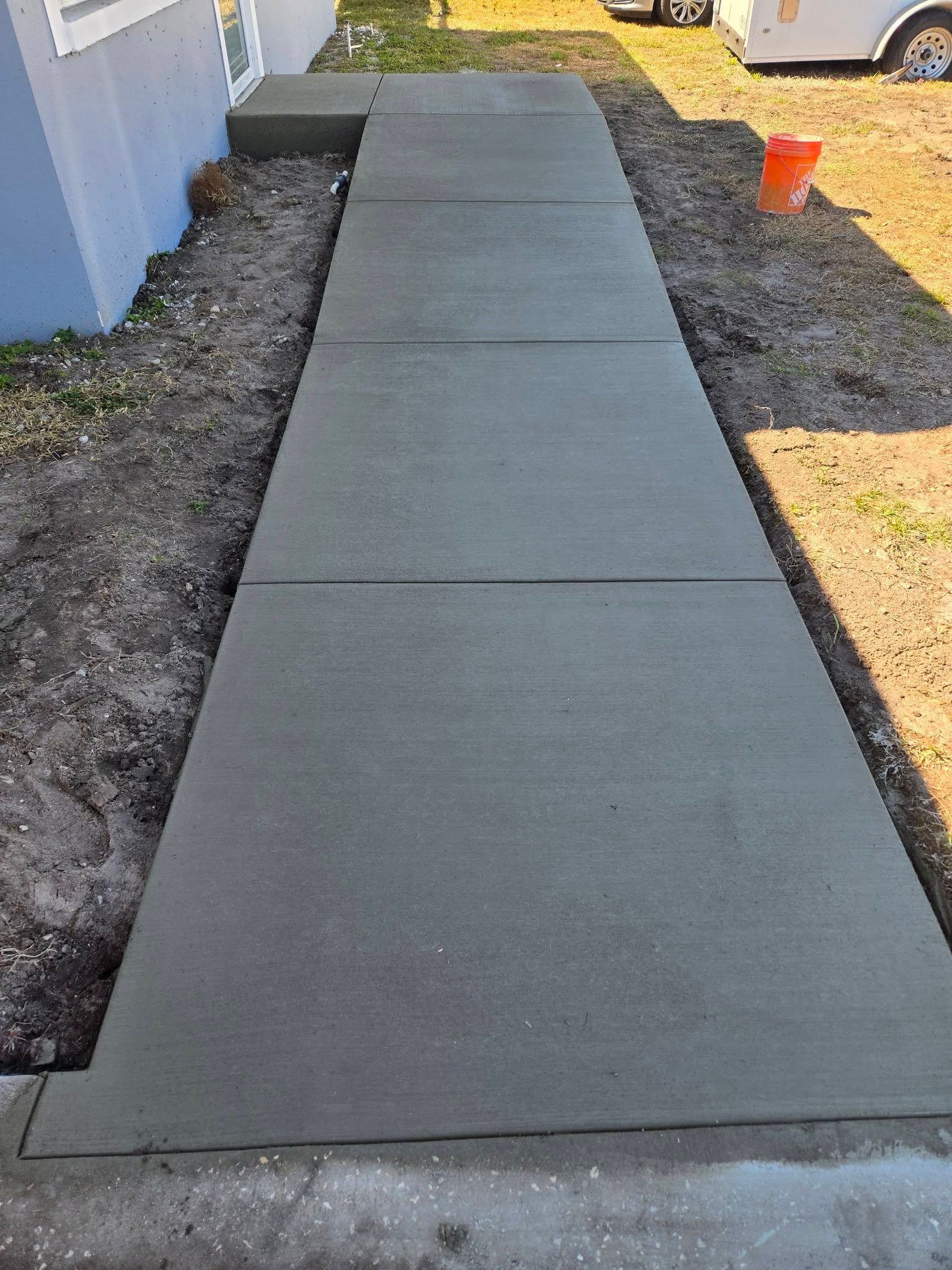 Concrete sidewalk beside a building, with gravel edges and a small orange cone in the distance. Concrete sidewalk beside a building, with gravel edges and a small orange cone in the distance.
