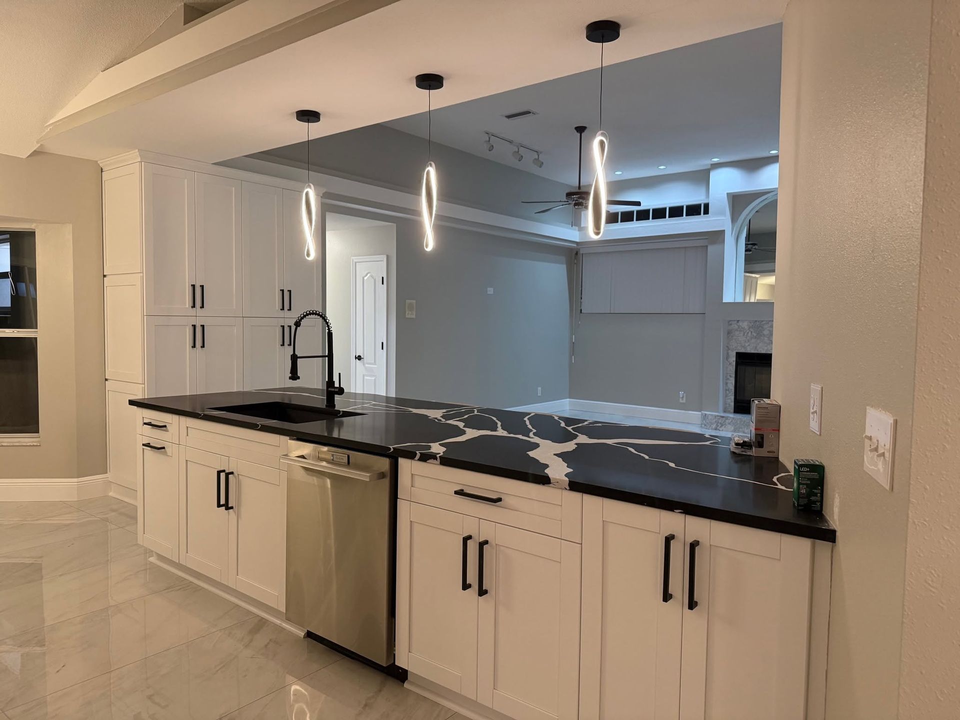 Modern white kitchen with black countertops, island sink, and pendant lights Modern white kitchen with black countertops, island sink, and pendant lights