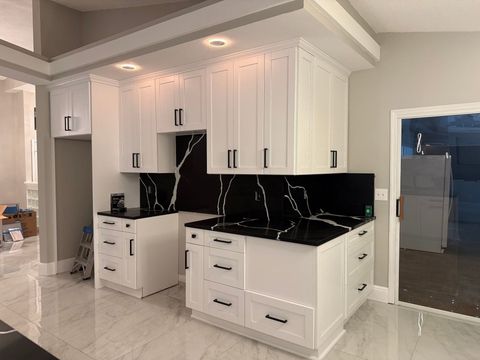 Modern white kitchen with black countertops, black backsplash, and glossy tile floor Modern white kitchen with black countertops, black backsplash, and glossy tile floor