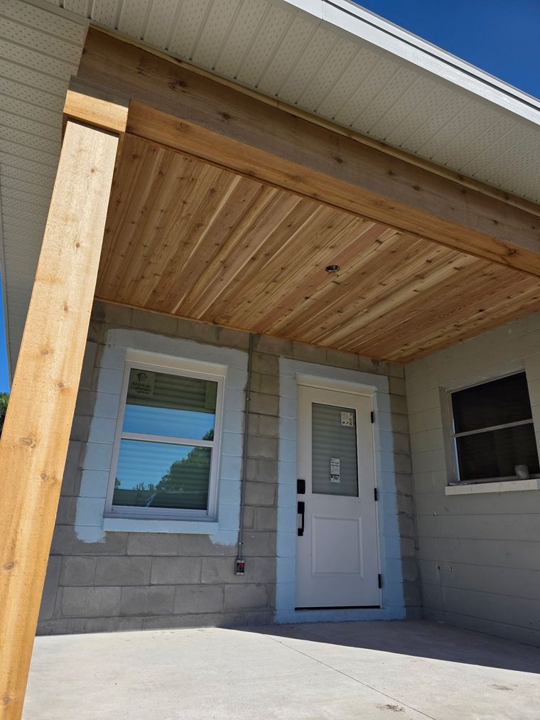 Front porch with wood ceiling, white door, and two windows on a stone exterior wall. Front porch with wood ceiling, white door, and two windows on a stone exterior wall.