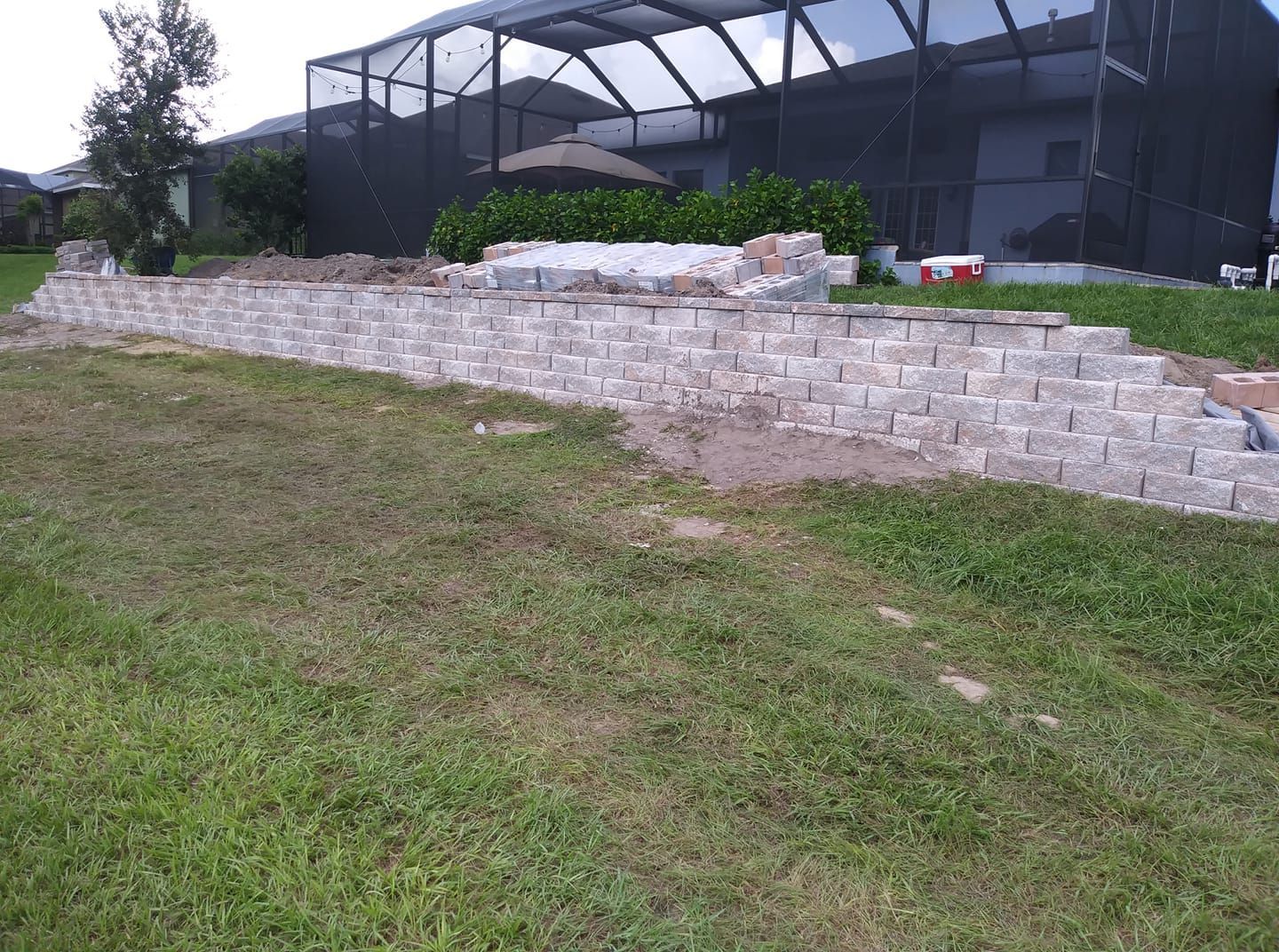 Grassy slope in front of a stone retaining wall and black netted structure in a park or sports area