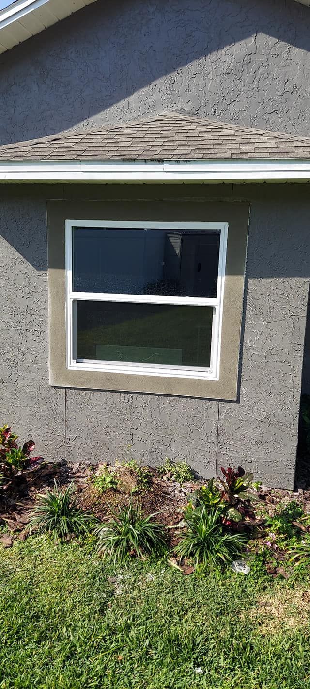 White-trimmed window on a gray stucco house above a small flower bed and grass.