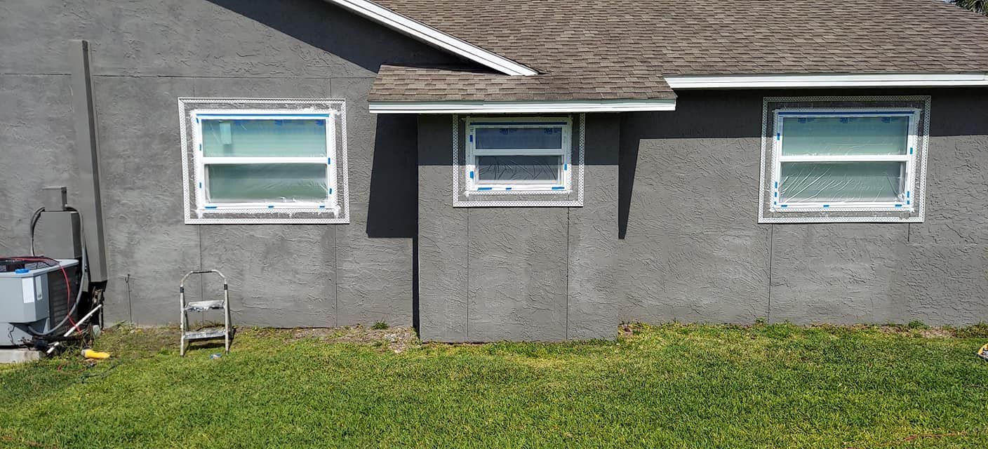 Gray house exterior with three windows and a grassy lawn in front