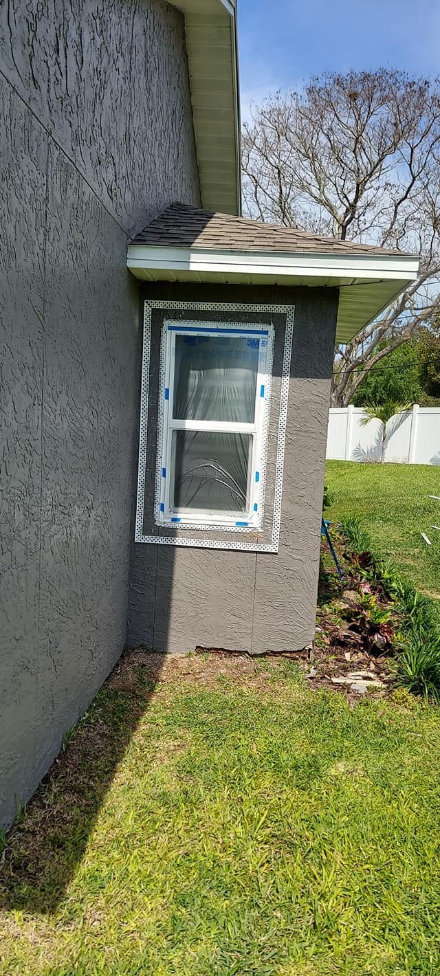 Small side window in a stucco wall beside a grassy yard and trees under a clear blue sky