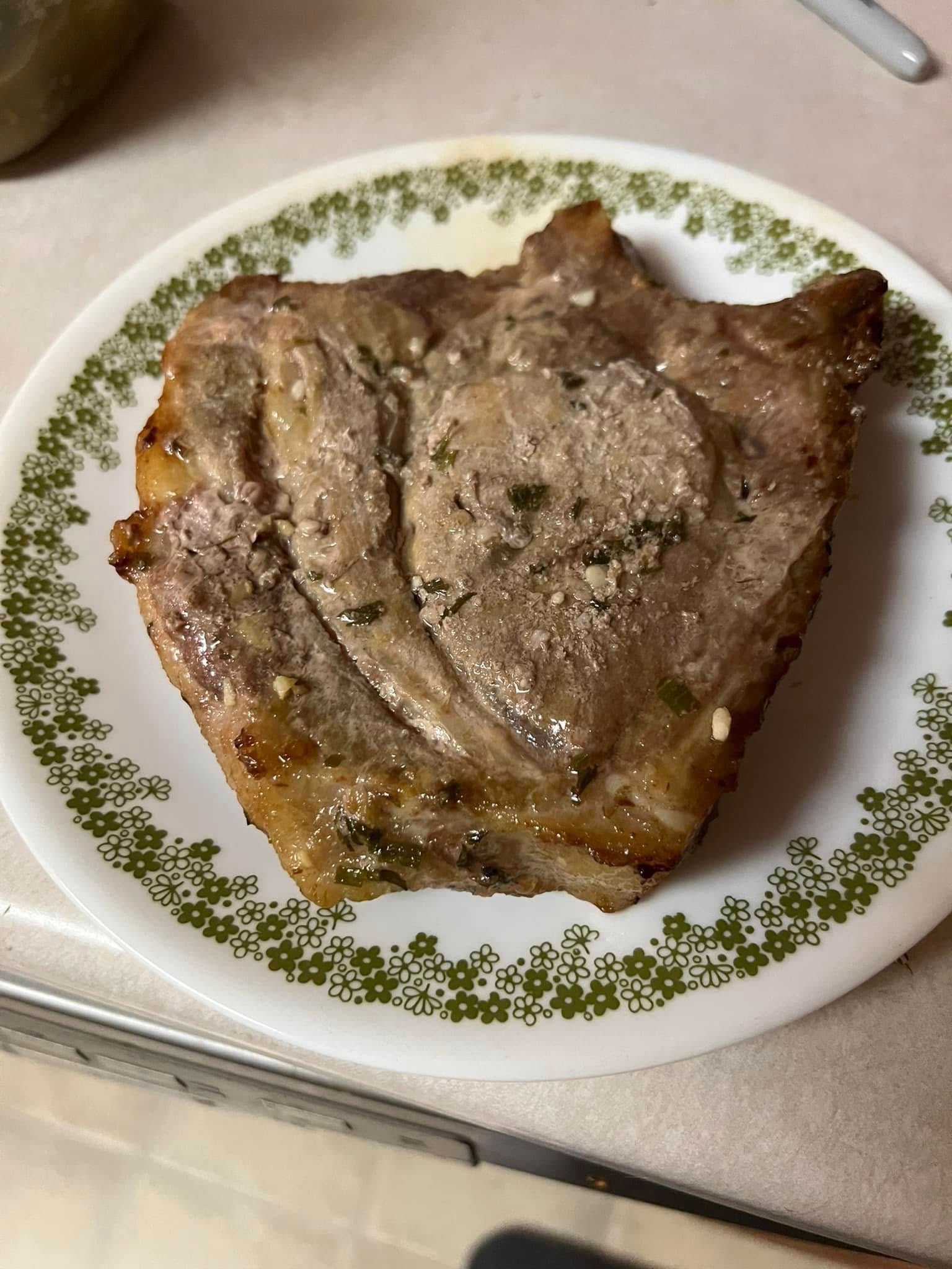 Cooked steak on a white plate with a green floral border on a kitchen counter