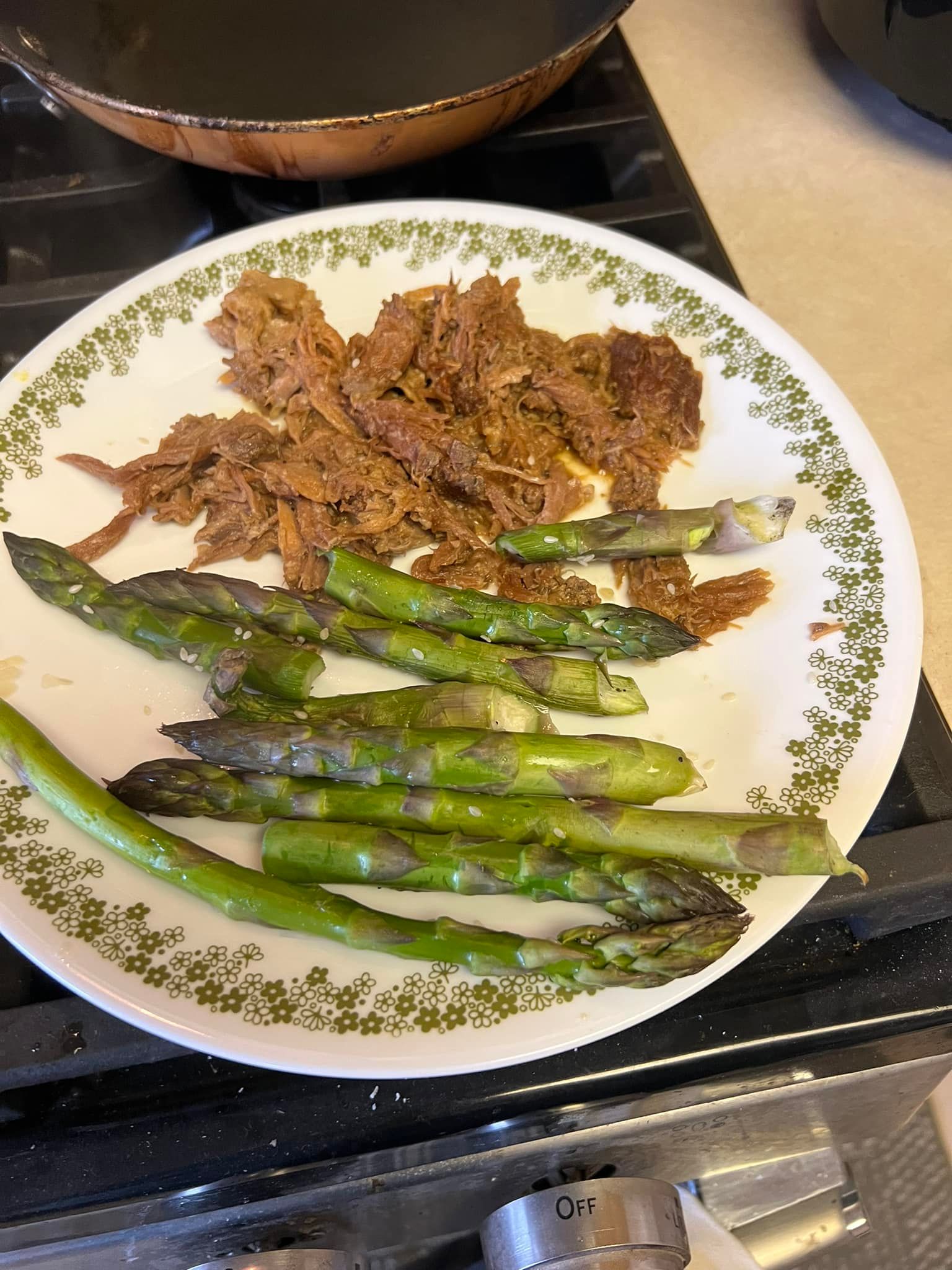 Plate of roasted asparagus with shredded meat on a stovetop.