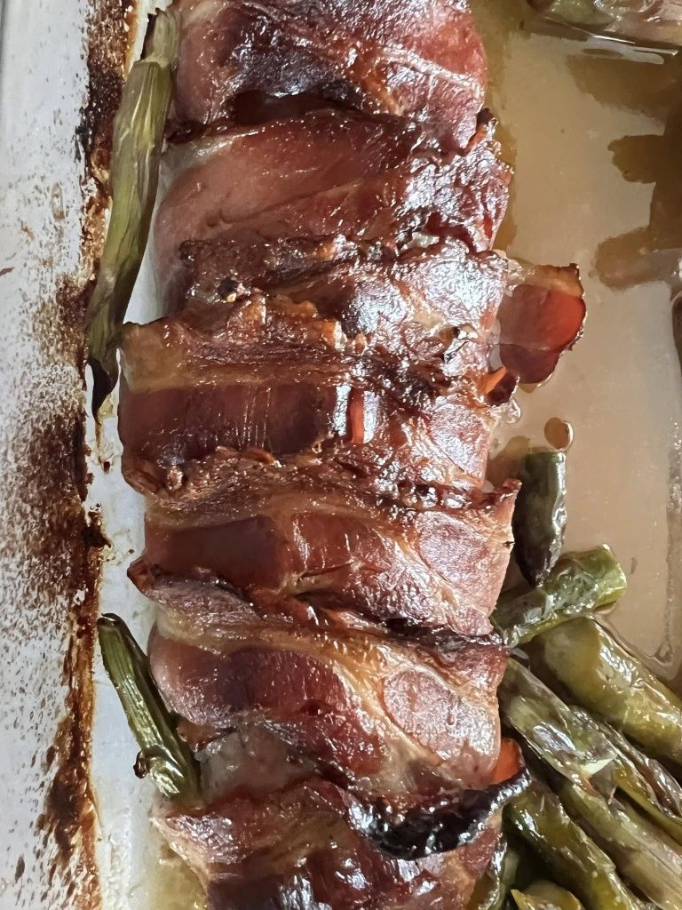 Sliced roasted meat wrapped in bacon, served with green beans on a white plate.