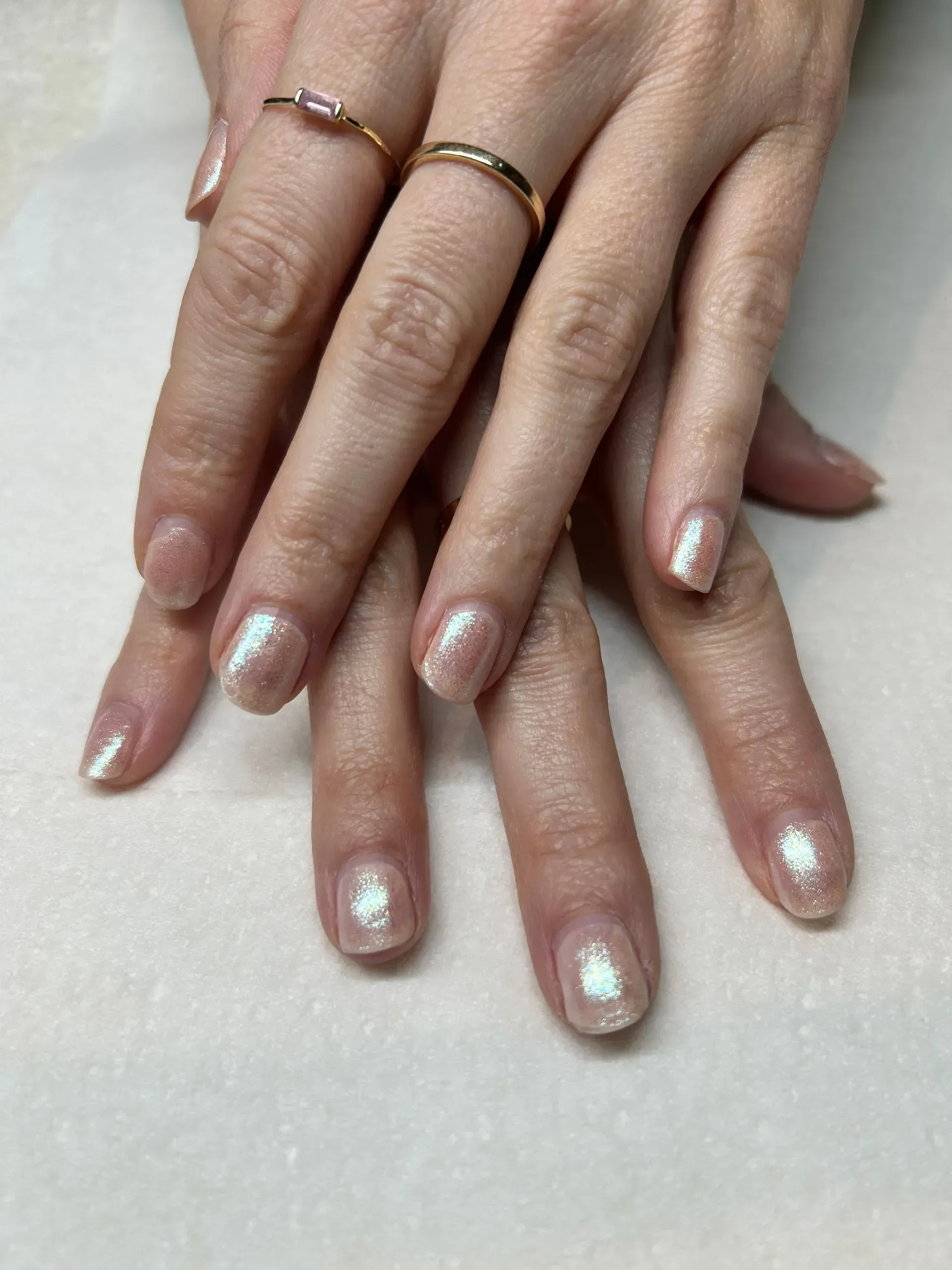 Hands with light pink iridescent nail polish, and gold rings. Hands with light pink iridescent nail polish, and gold rings.
