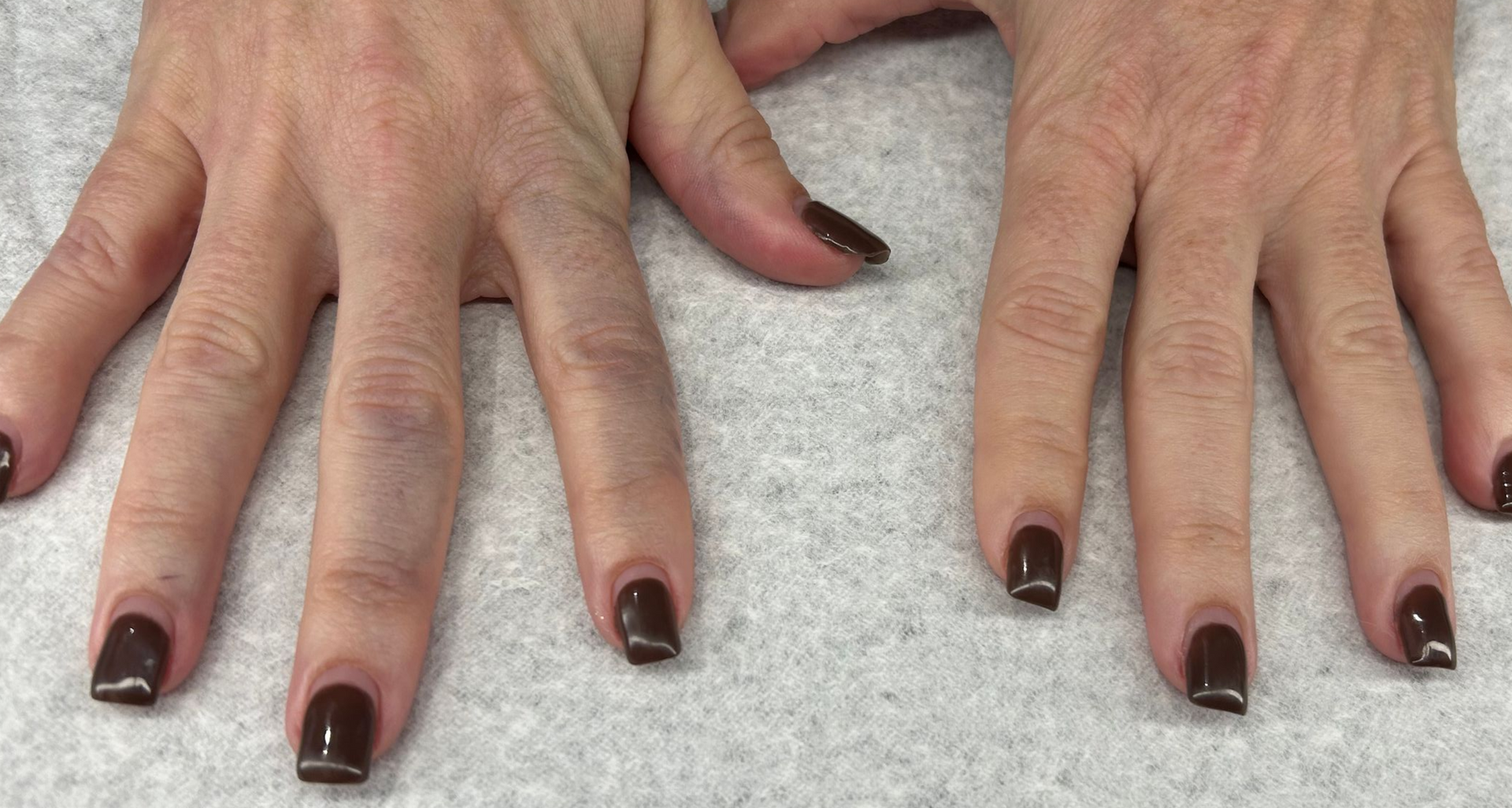 Two hands with brown nail polish on fingers. Skin is fair with visible veins.