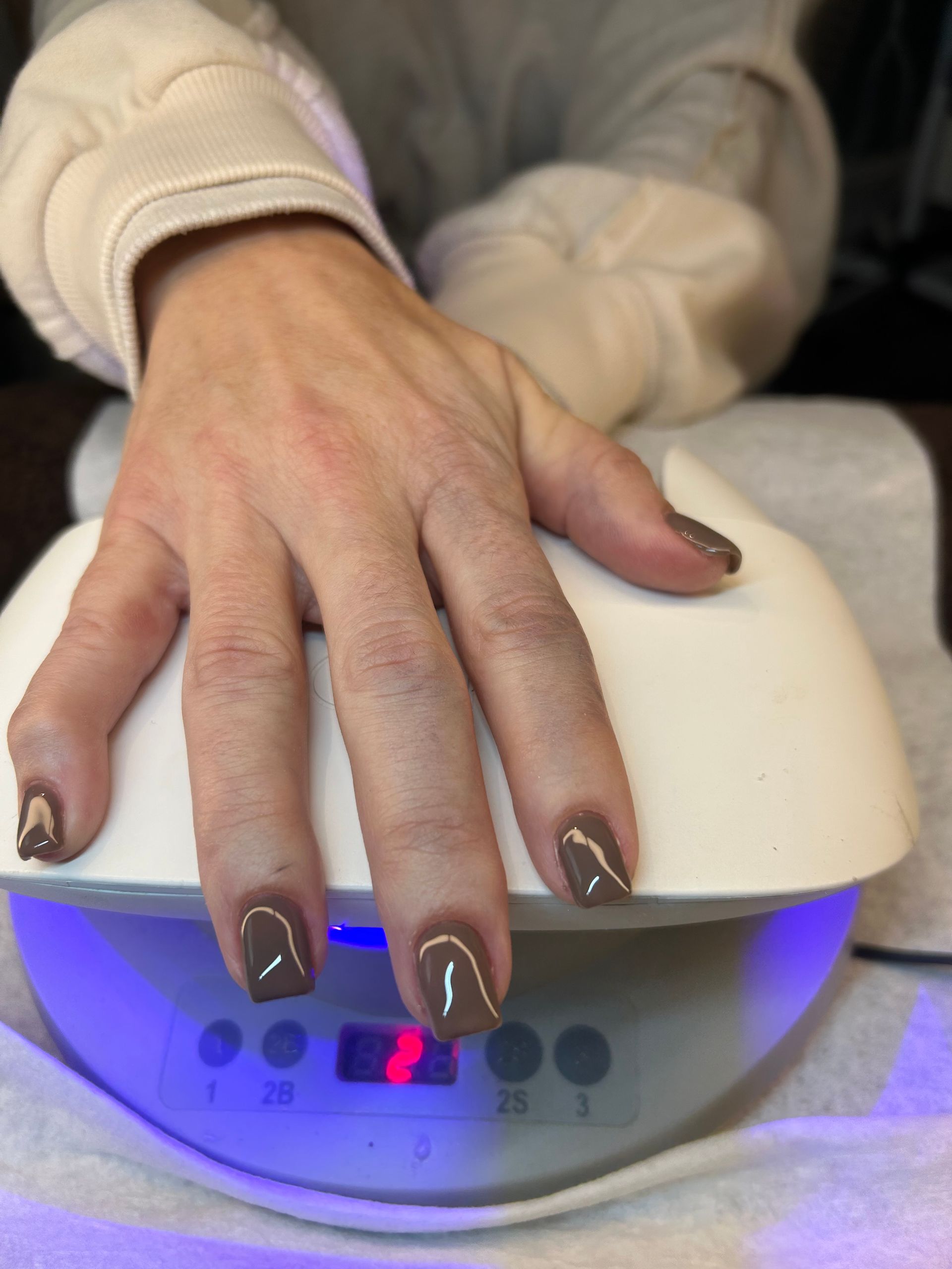 Hand with brown nails in a UV nail lamp, lit by blue light.