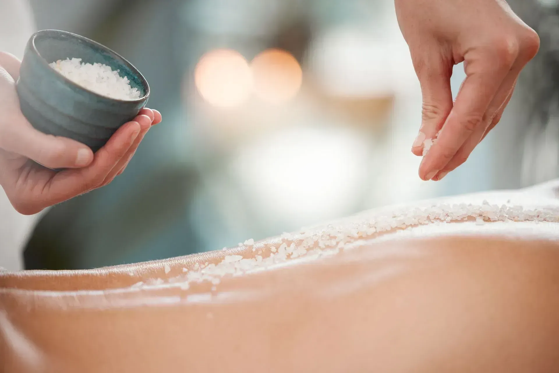 Person receiving salt scrub treatment on their back; hands pouring salt. Person receiving salt scrub treatment on their back; hands pouring salt.