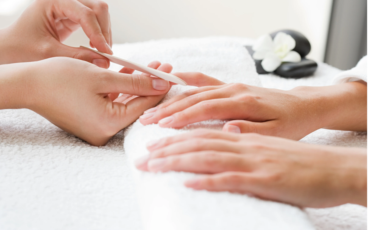 Manicurist filing a person's fingernails, hands resting on a white towel. Manicurist filing a person's fingernails, hands resting on a white towel.