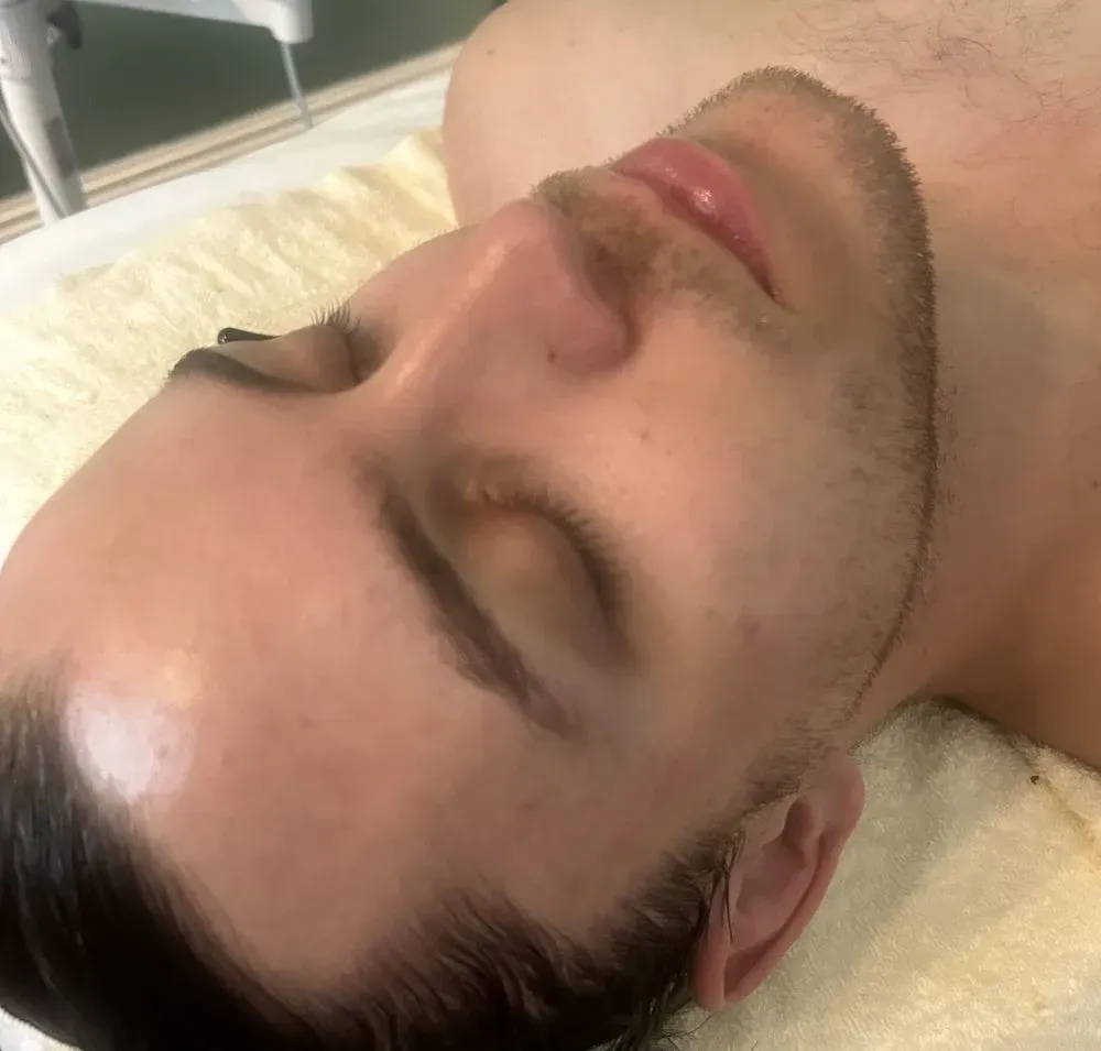 Close-up of a man lying on a towel with eyes closed, face turned up for a facial in a spa