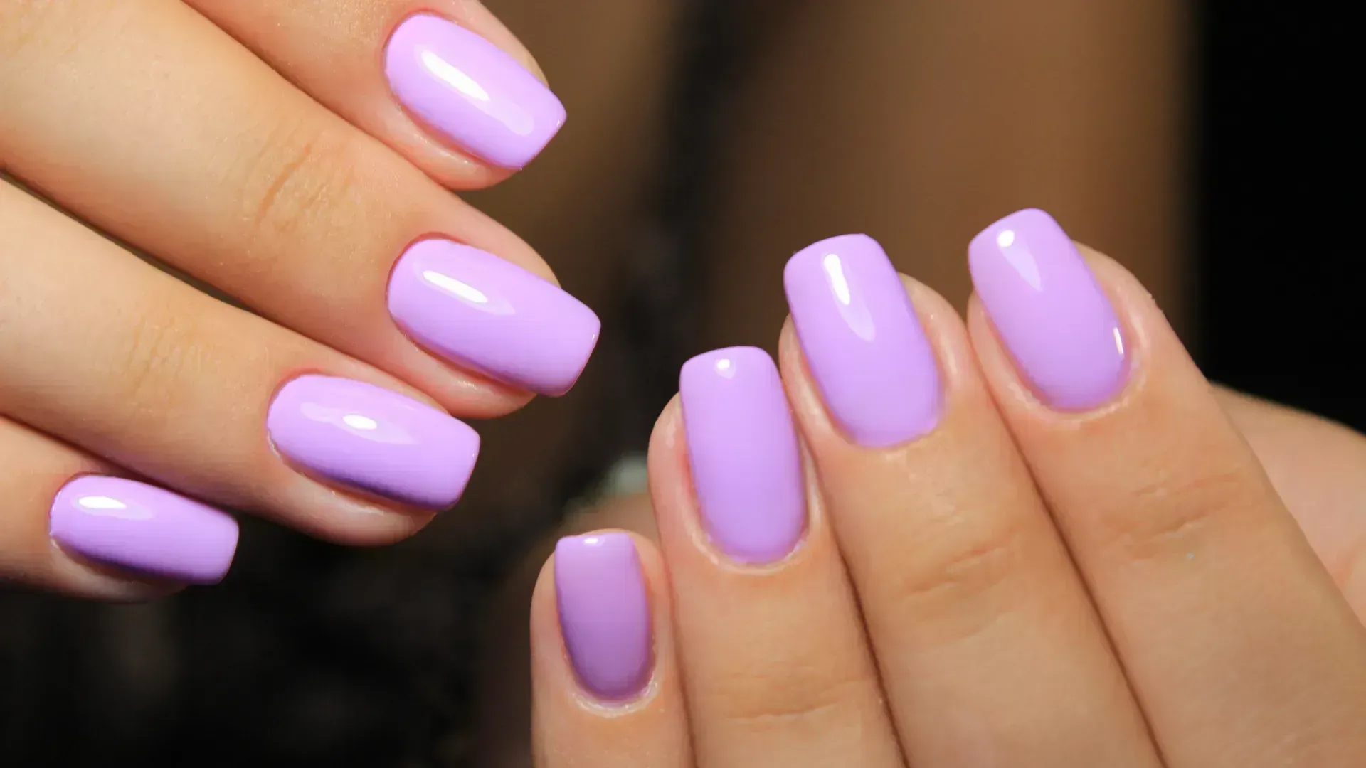 Hands with lavender-colored, square-shaped manicured nails.