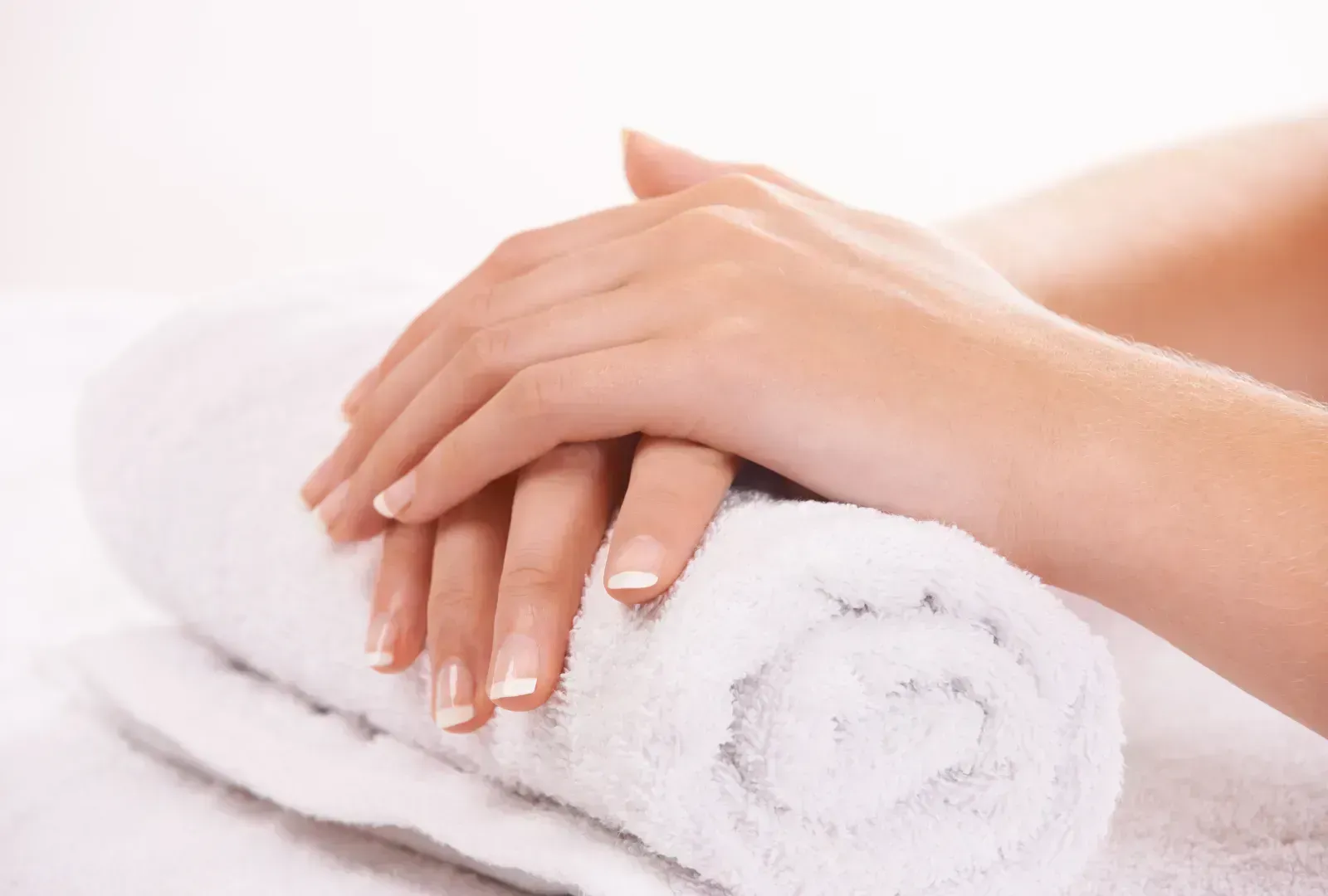 Hands with French manicured nails resting on a rolled white towel. Hands with French manicured nails resting on a rolled white towel.